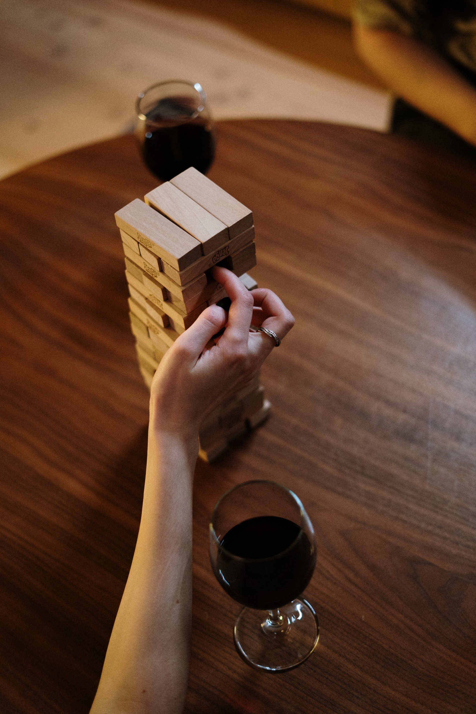 A person is playing jenga with a glass of wine on a wooden table.