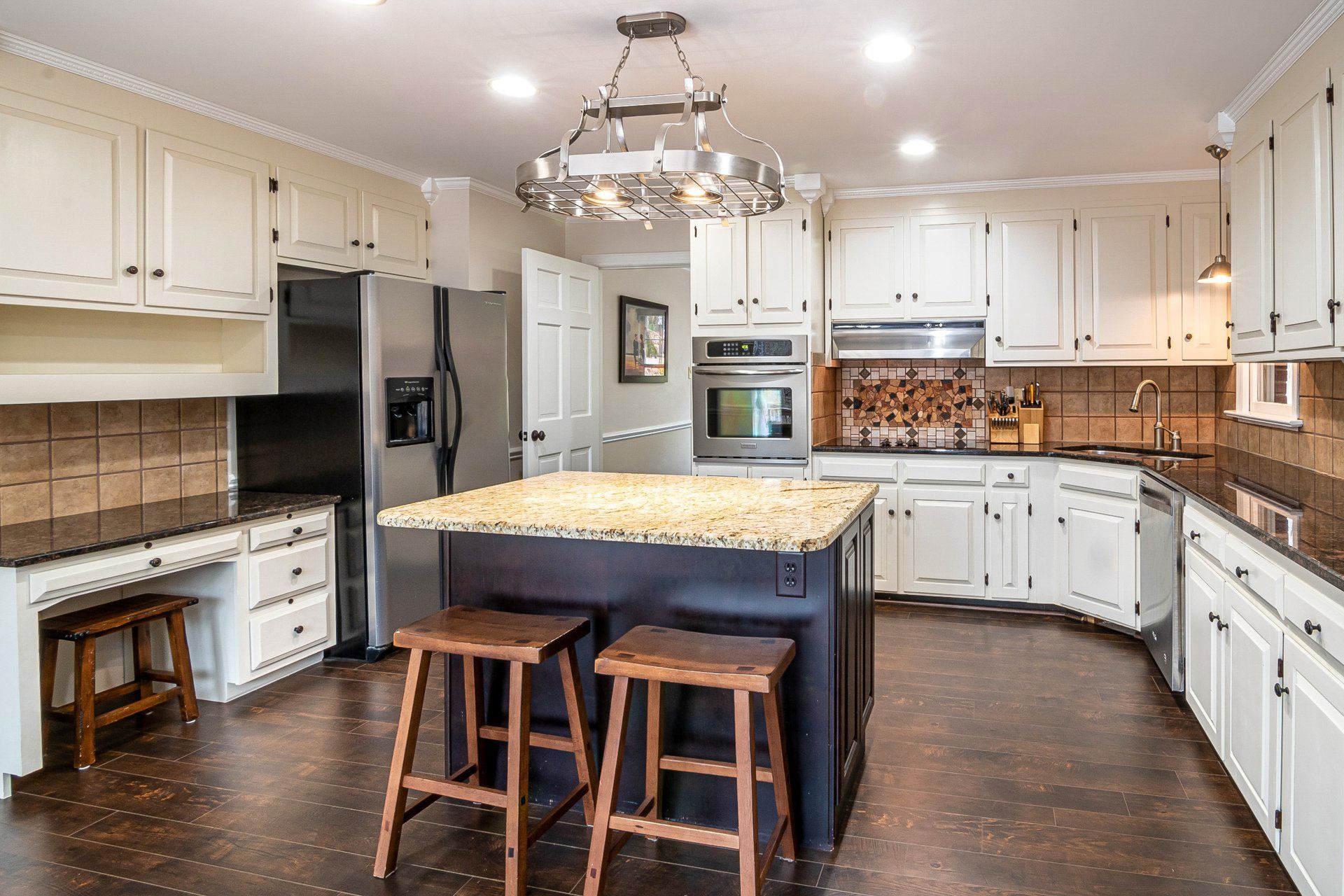 A kitchen with white cabinets , stools , a refrigerator , and a large island.