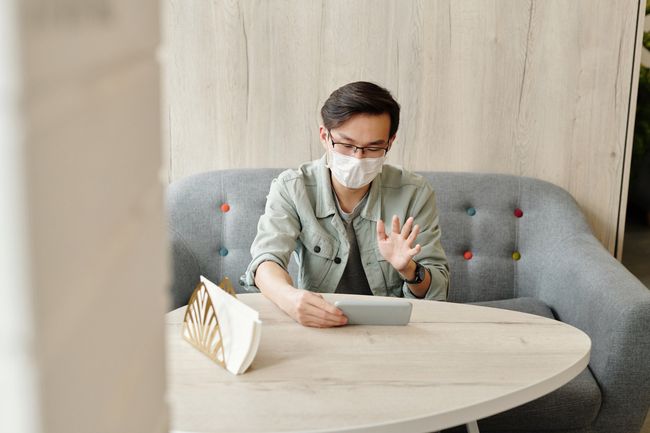 Masked person waving at a table in a bright room