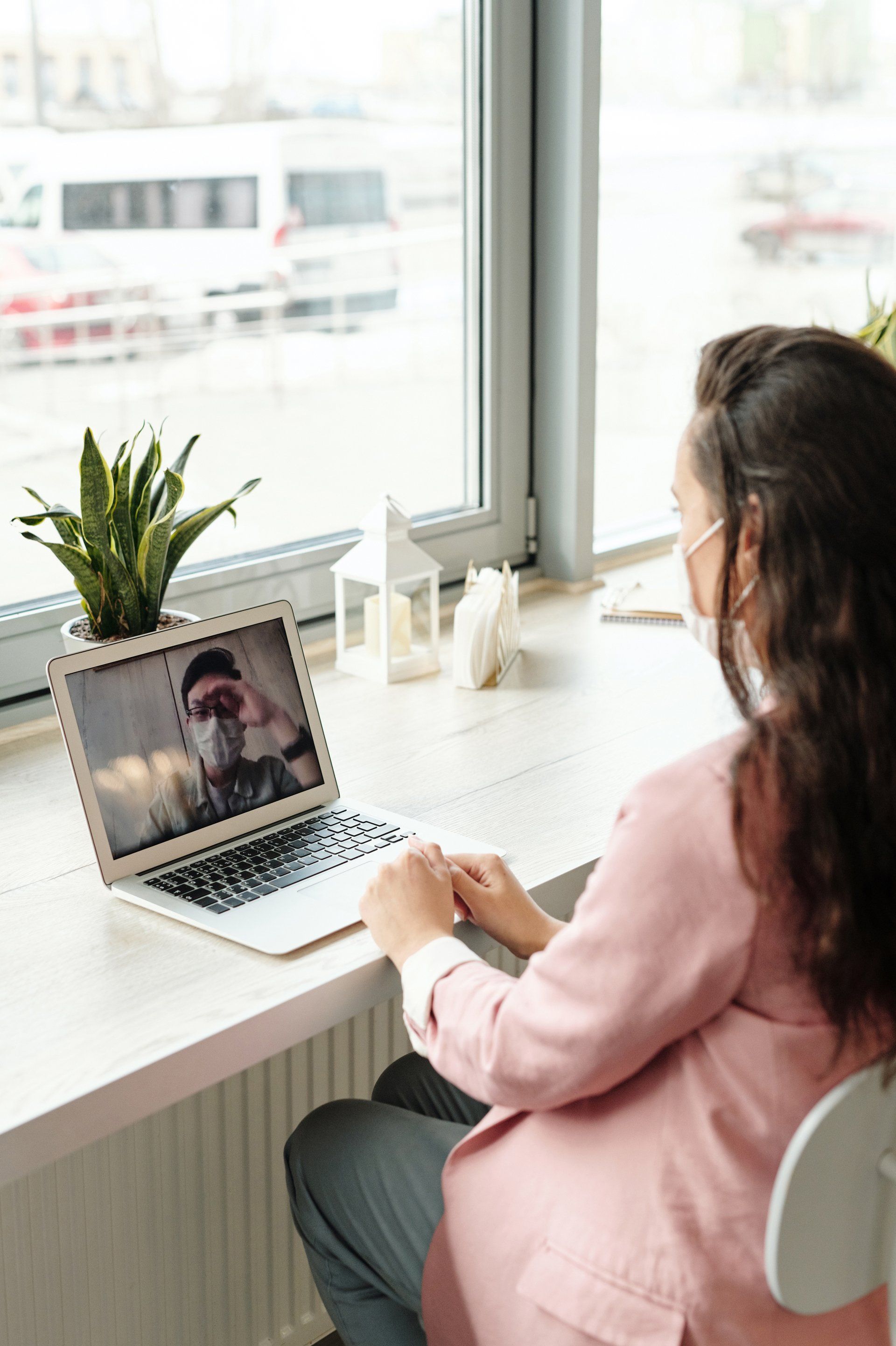 A woman wearing a mask is sitting in front of a laptop computer.