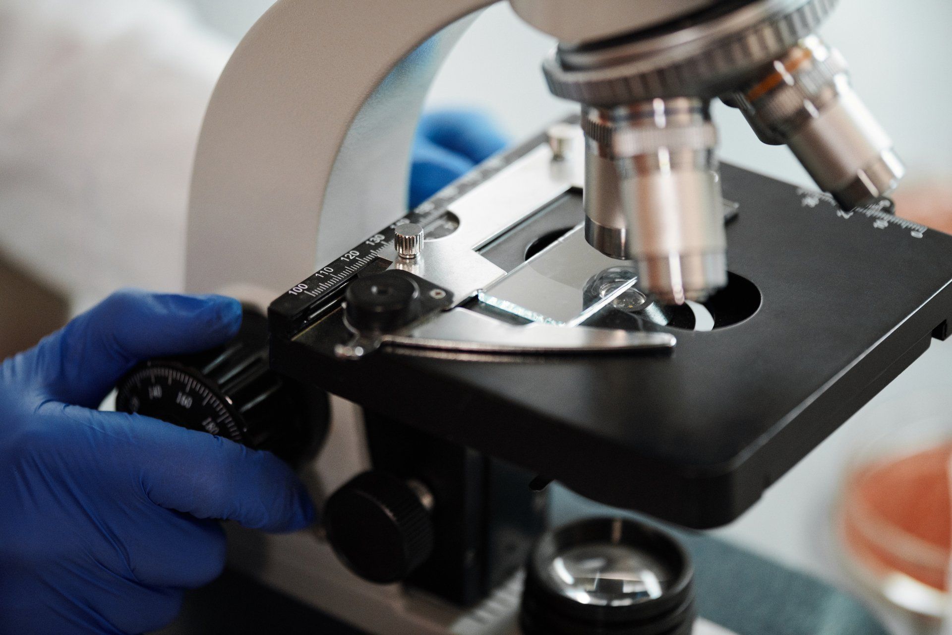 A person wearing blue gloves is looking through a microscope.