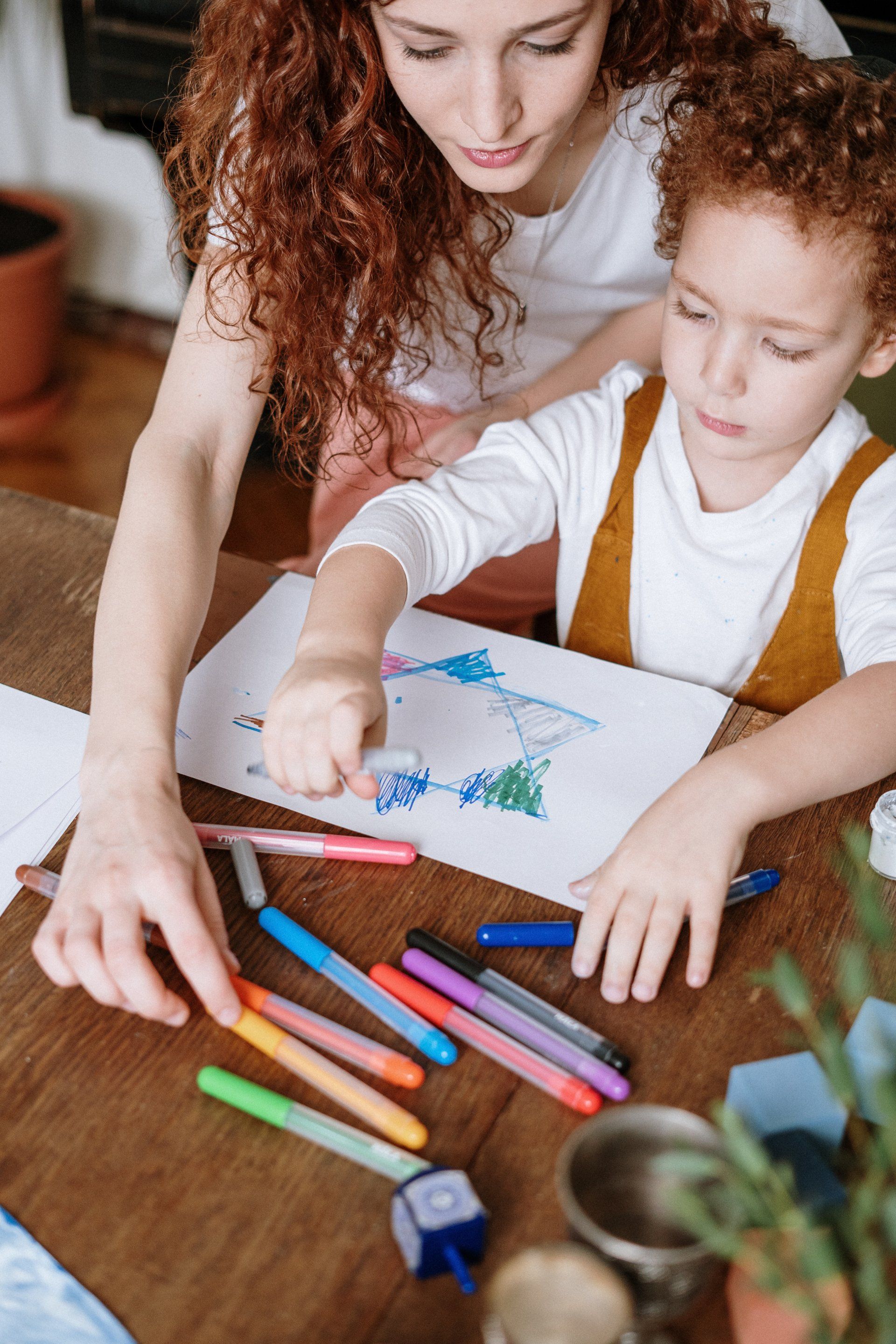 A woman and child are sitting at a table drawing with markers.
