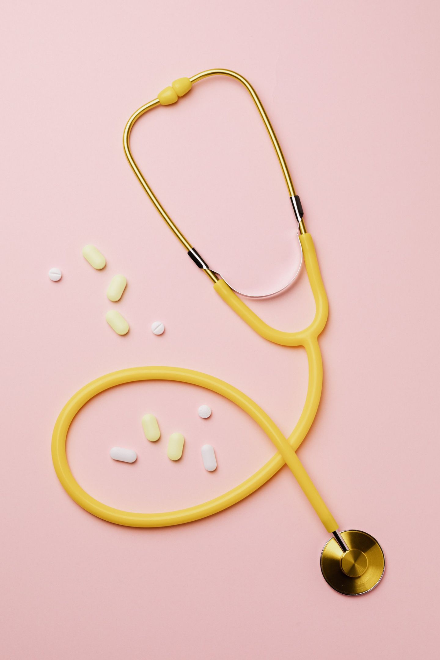 A yellow stethoscope is surrounded by pills on a pink background