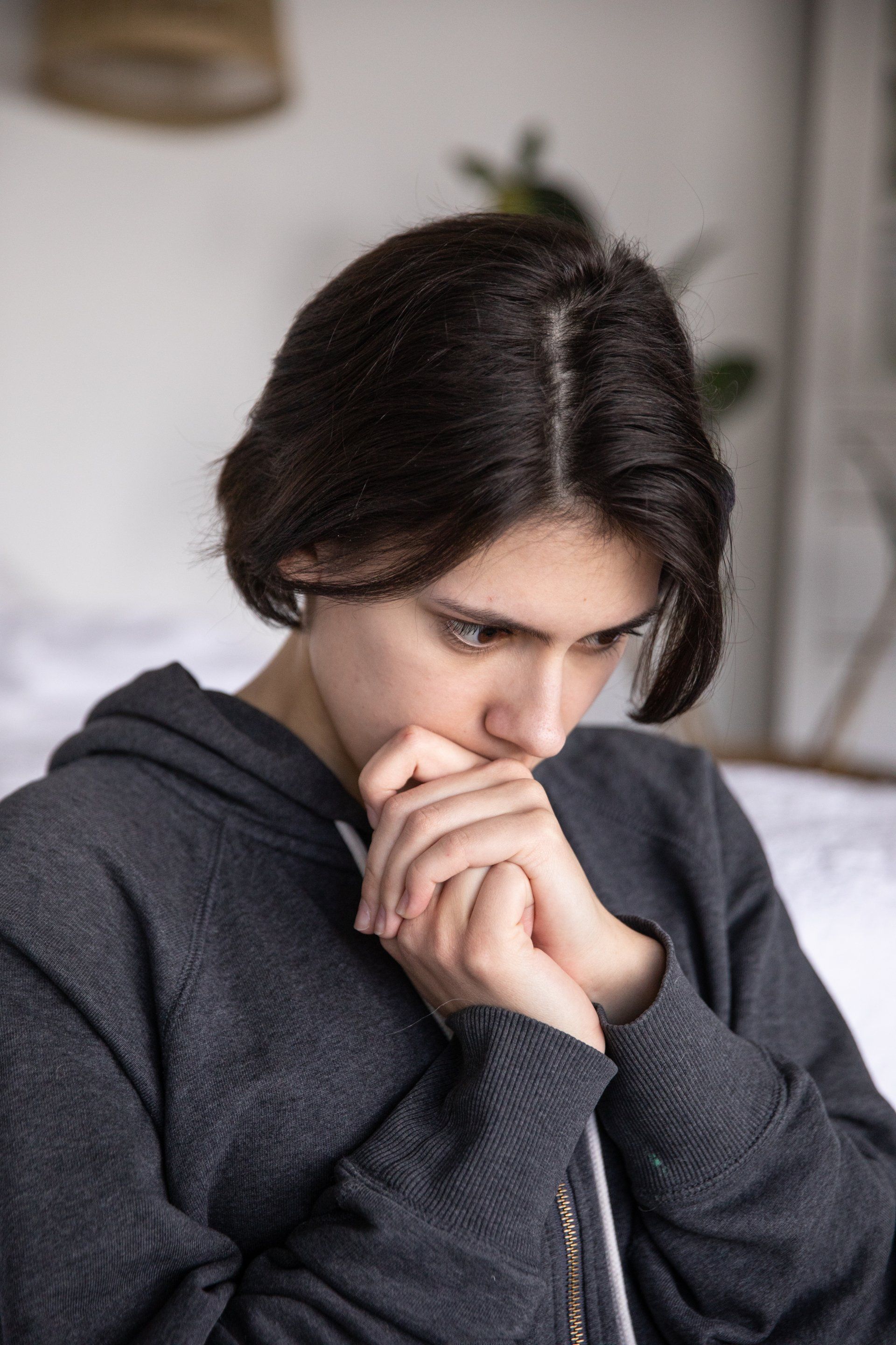 A young woman is sitting on a bed with her hands on her face.