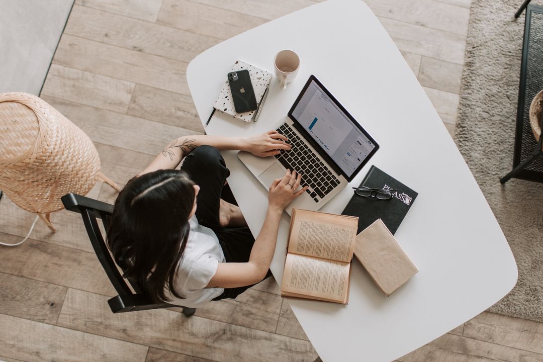 Image of a woman looking at books and typing on her computer