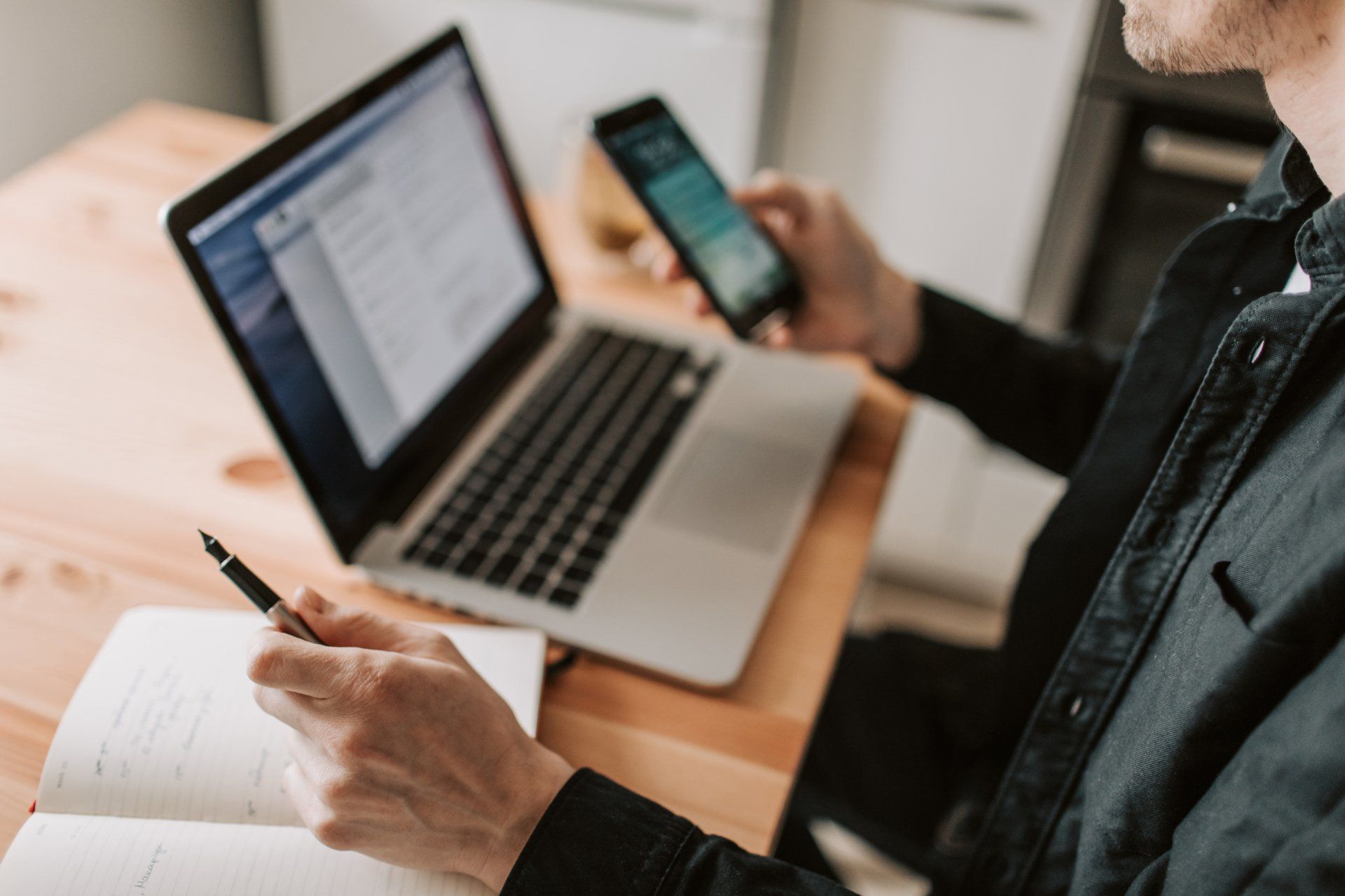A man is sitting at a desk using a laptop and a cell phone.