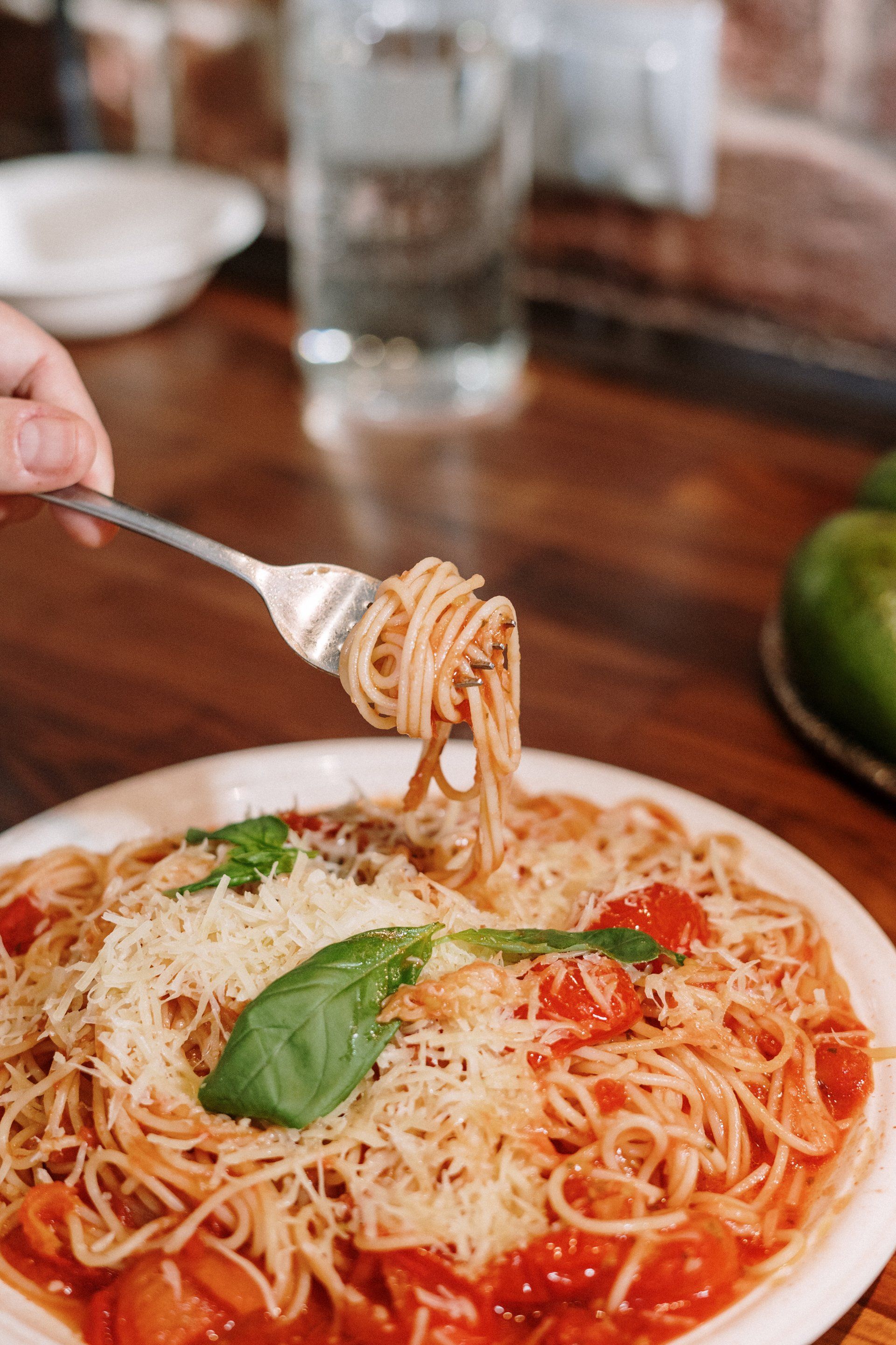 A person is eating spaghetti with tomato sauce and cheese with a fork with oregano on top