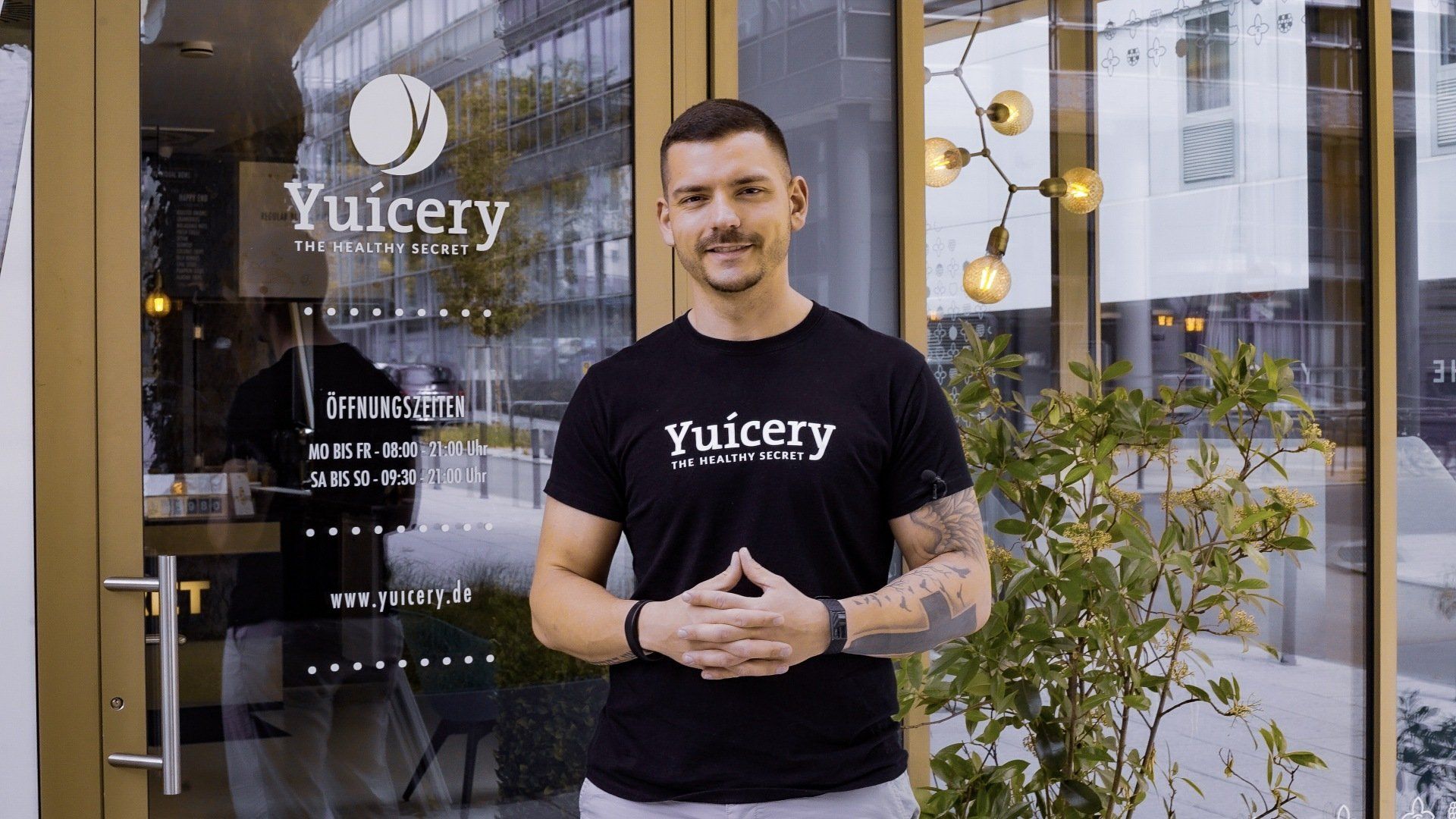 A man in a black t-shirt is standing in front of a glass door.
