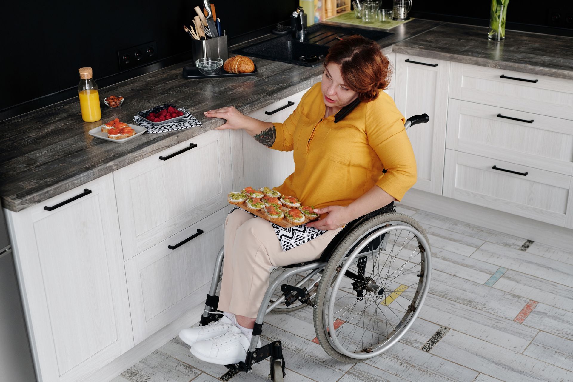 Person in a wheelchair in a bright kitchen, holding a plate of pastries at the counter.