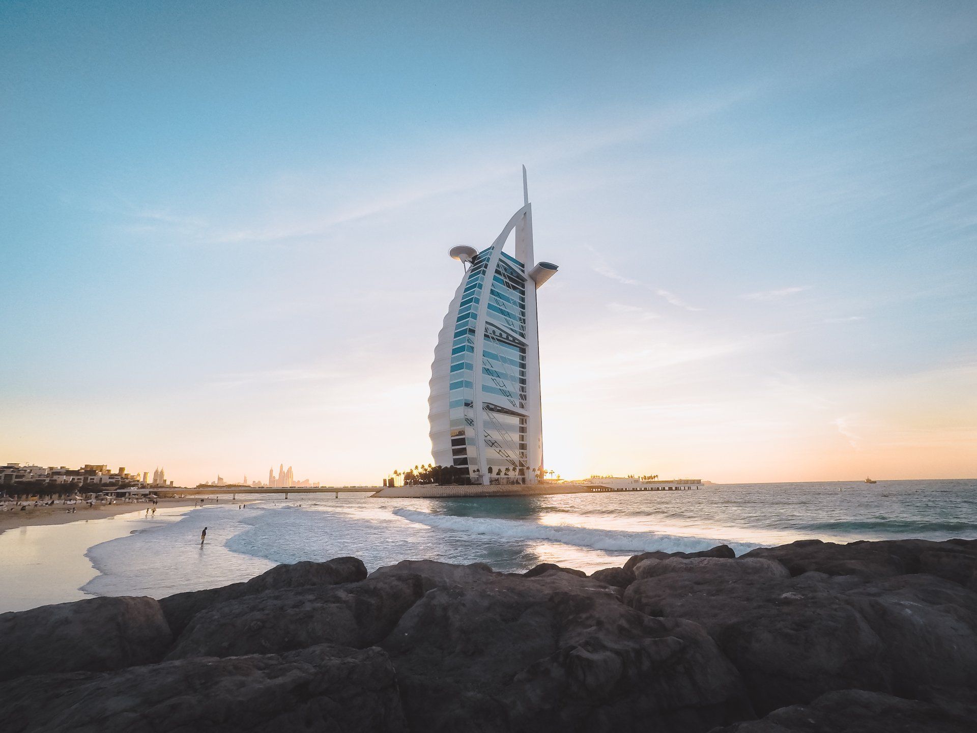 Burj Al Arab hotel in Dubai by the beach at sunset, with blue and orange sky and waves.