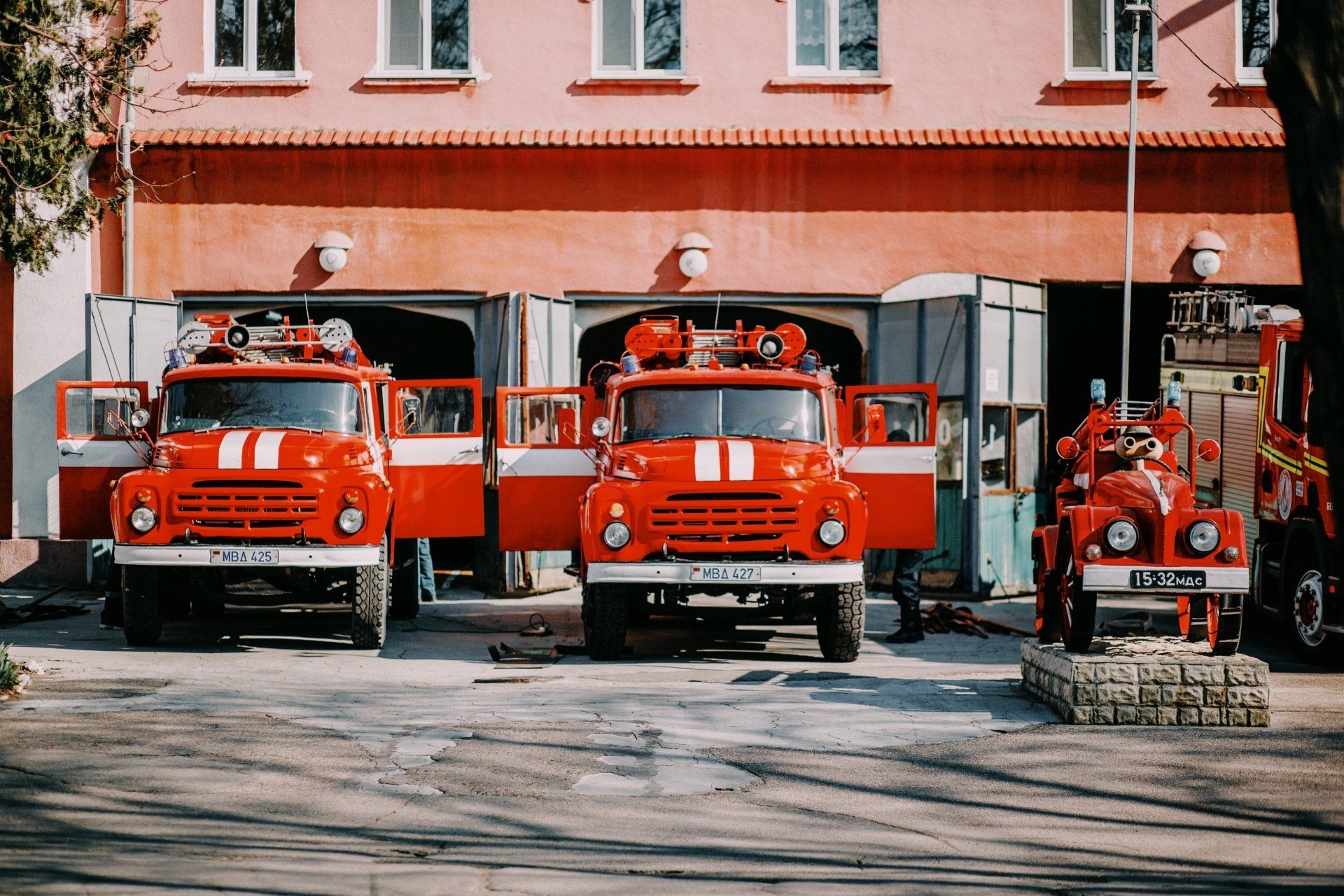 Three red fire trucks are parked in front of a fire station.