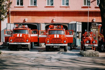 Three red fire trucks are parked in front of a fire station.