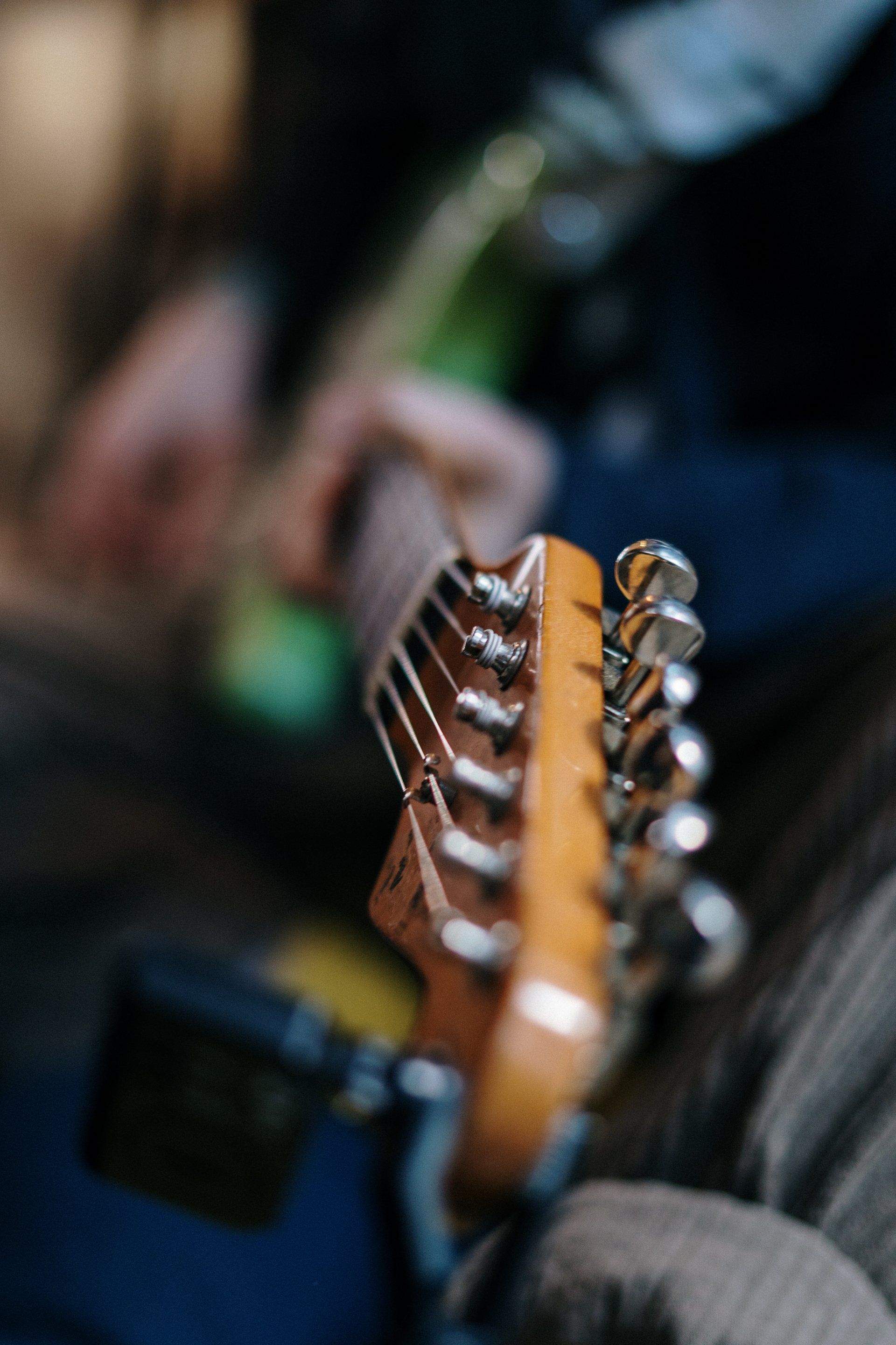 Close-up of a person playing a guitar, focusing on the tuning pegs and strings.
