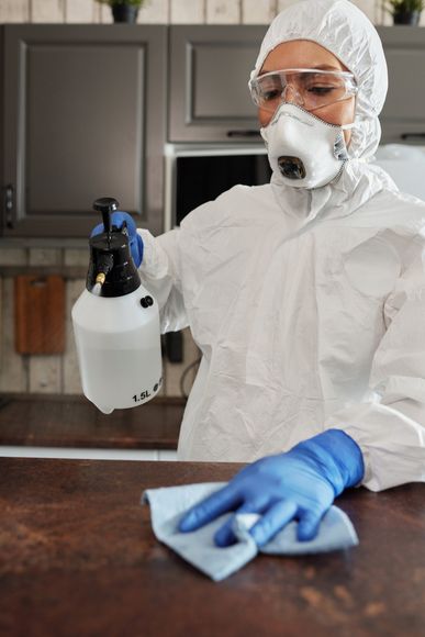 A woman in a protective suit is cleaning a counter in a kitchen.