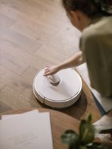 A woman is using a robot vacuum cleaner to clean the floor.