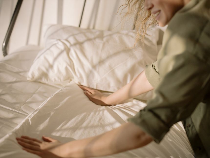 A woman is making a bed with white sheets and pillows.