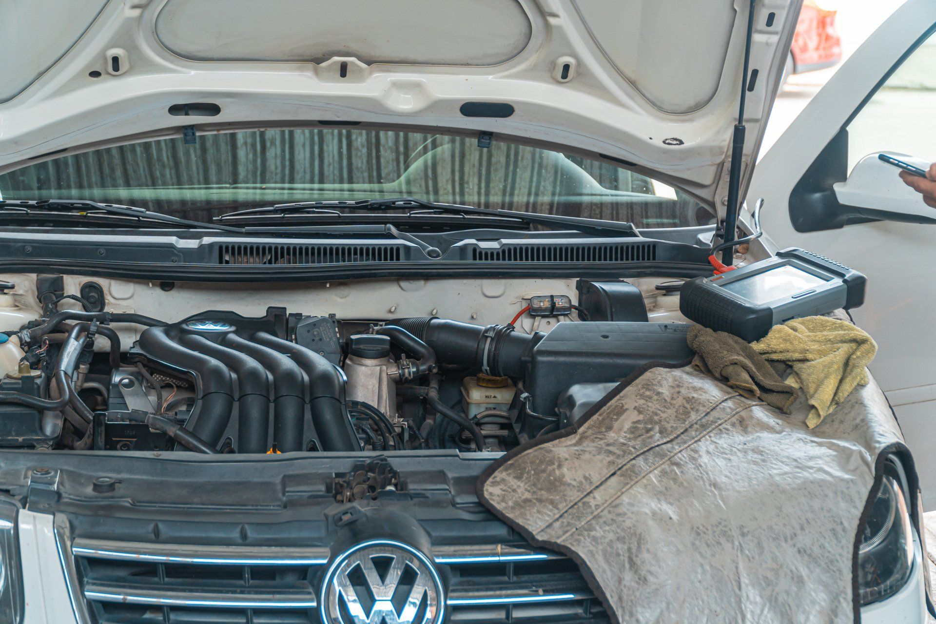 The hood of a white volkswagen is open and being worked on.