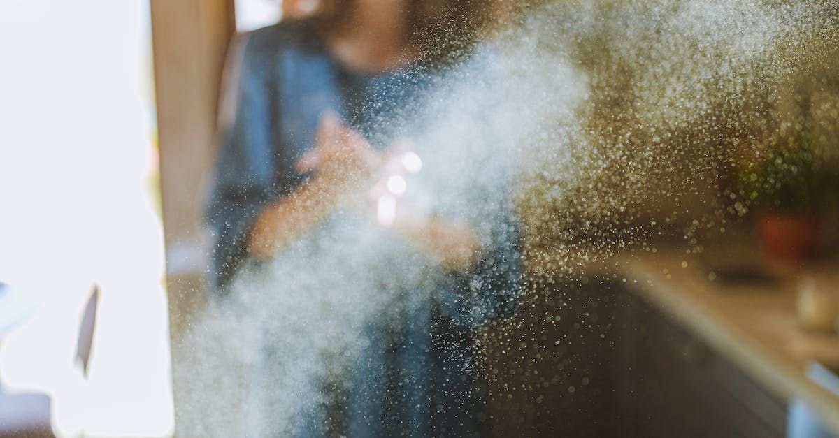 A woman is throwing flour in the air in a kitchen.