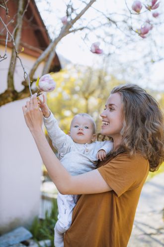 Eine Frau hält ein Baby und betrachtet eine Blume auf einem Baum.