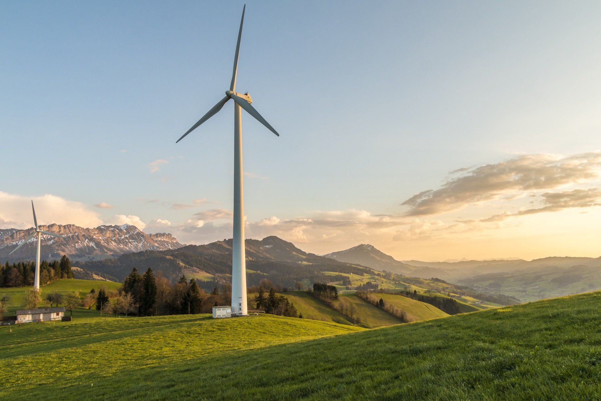 Two wind turbines are sitting on top of a grassy hill.
