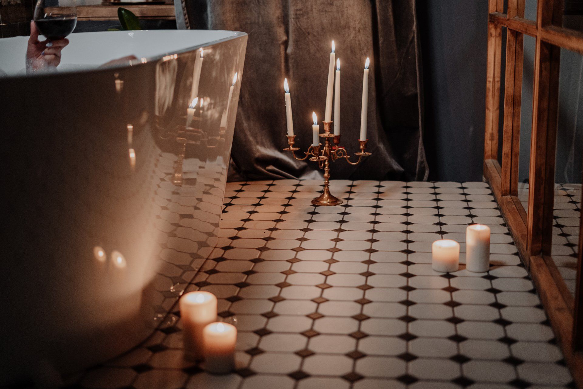 Spa-like bathroom with patterned tile floor, candles, dark drapery, and warm ambient lighting
