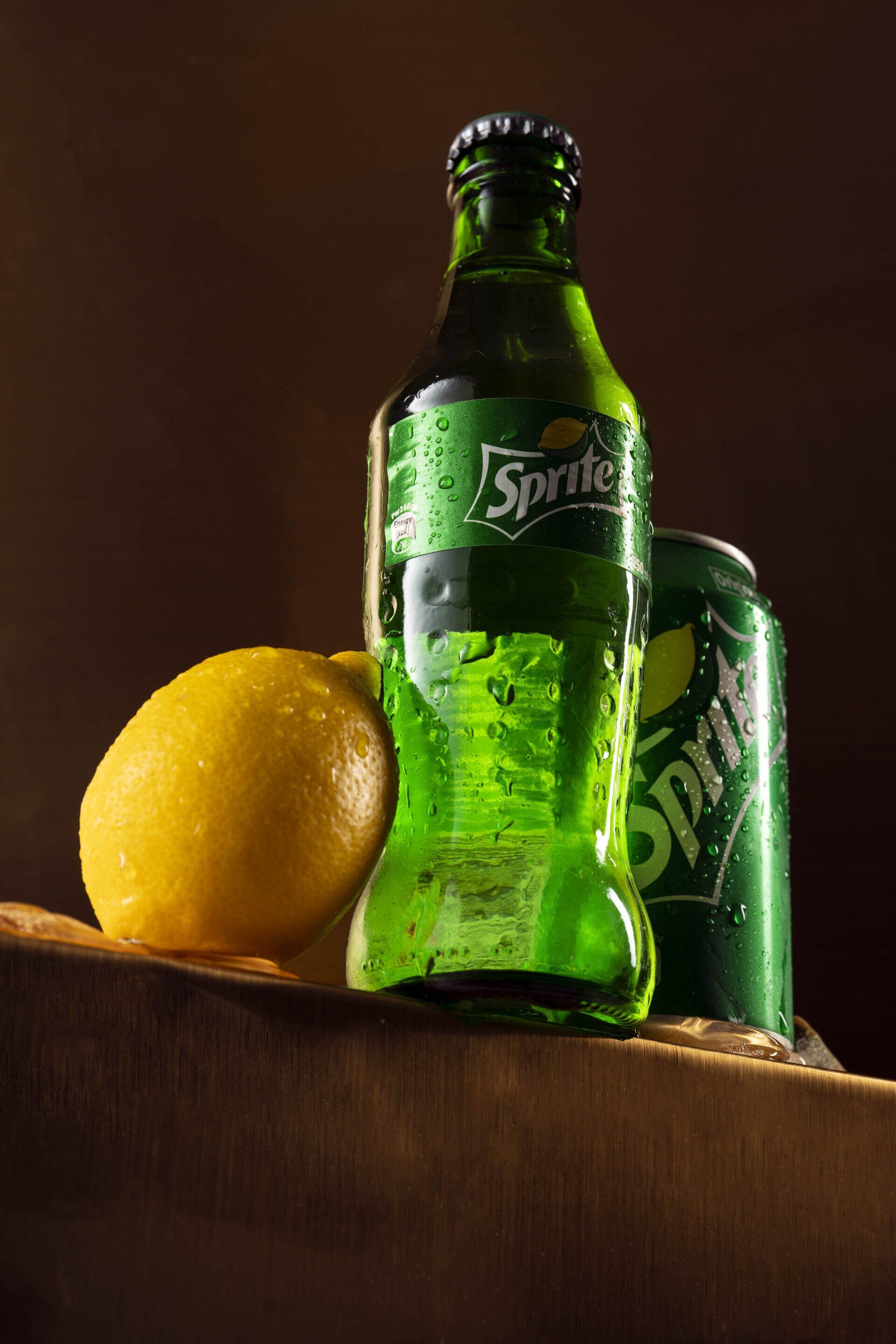 A bottle of sprite next to a can of sprite and a lemon.