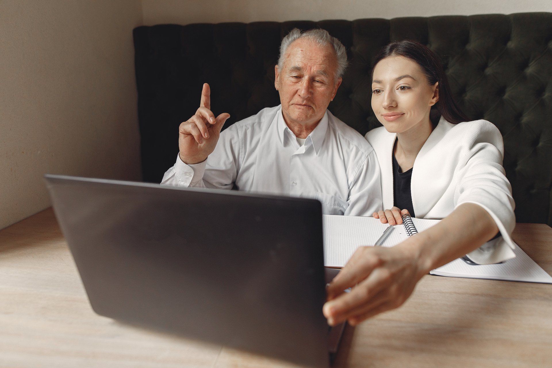An elderly man and a young woman are looking at a laptop computer.