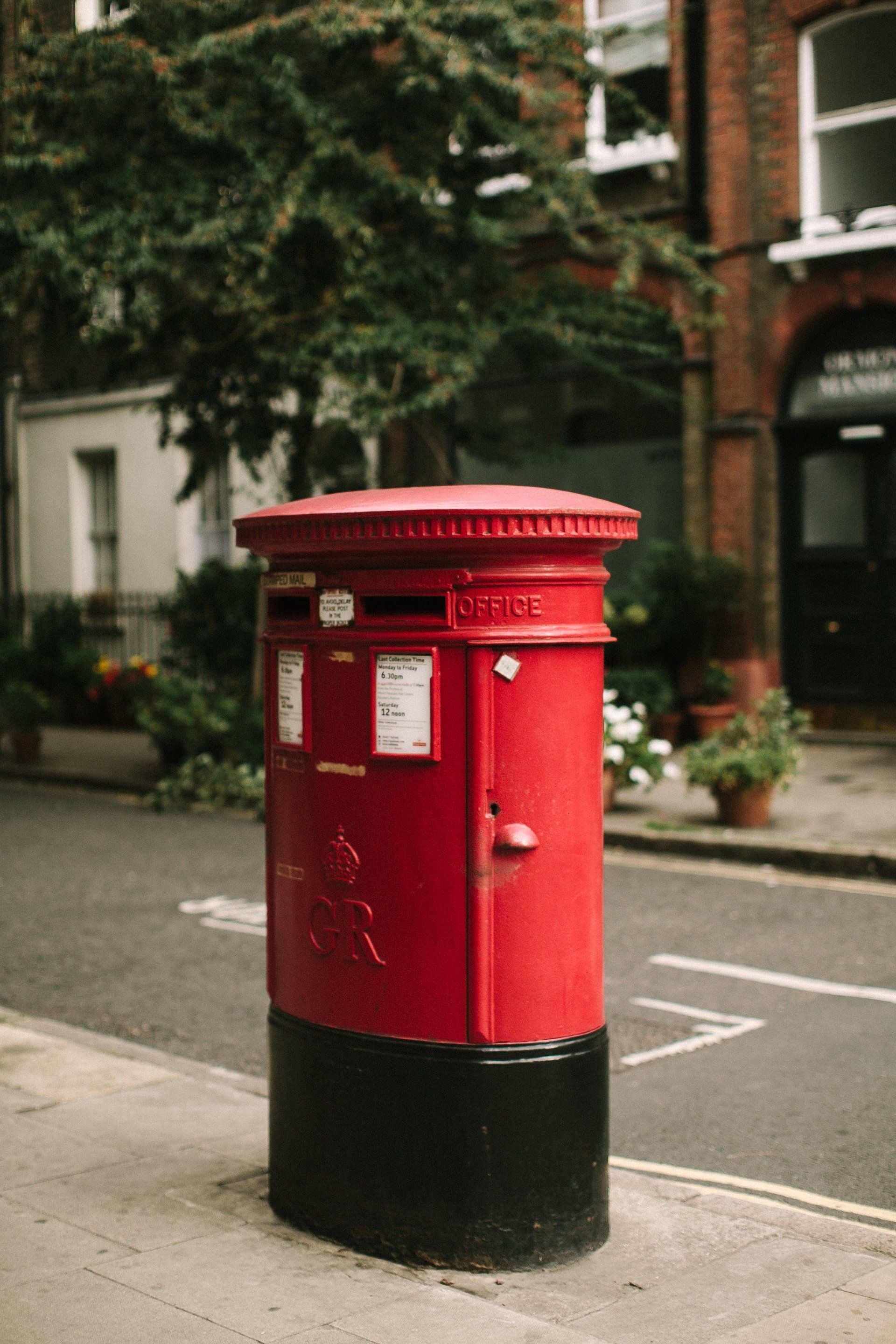 A red and black post box is sitting on the side of the road.