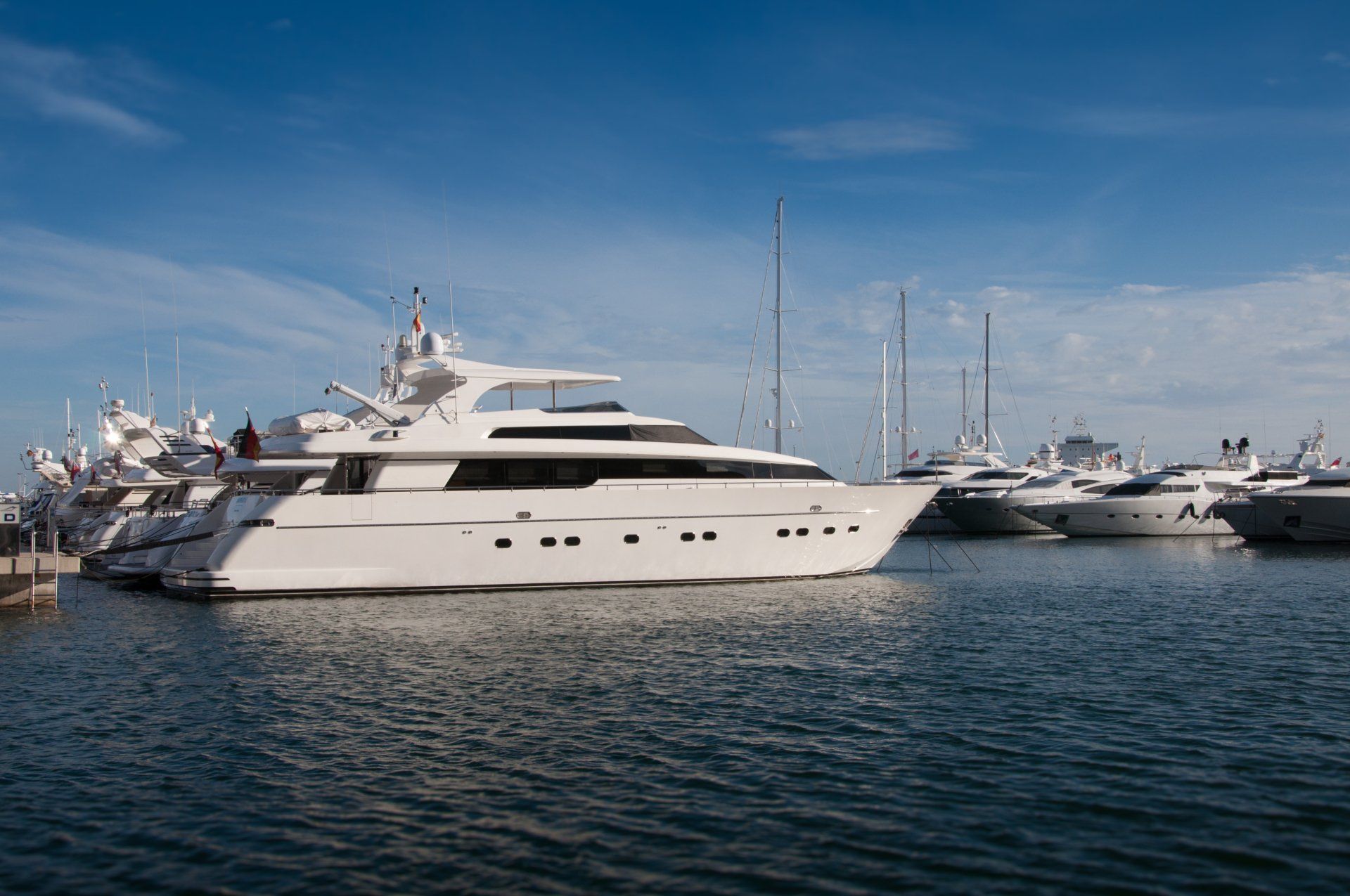 White yachts docked in a harbor with a blue sky and water.