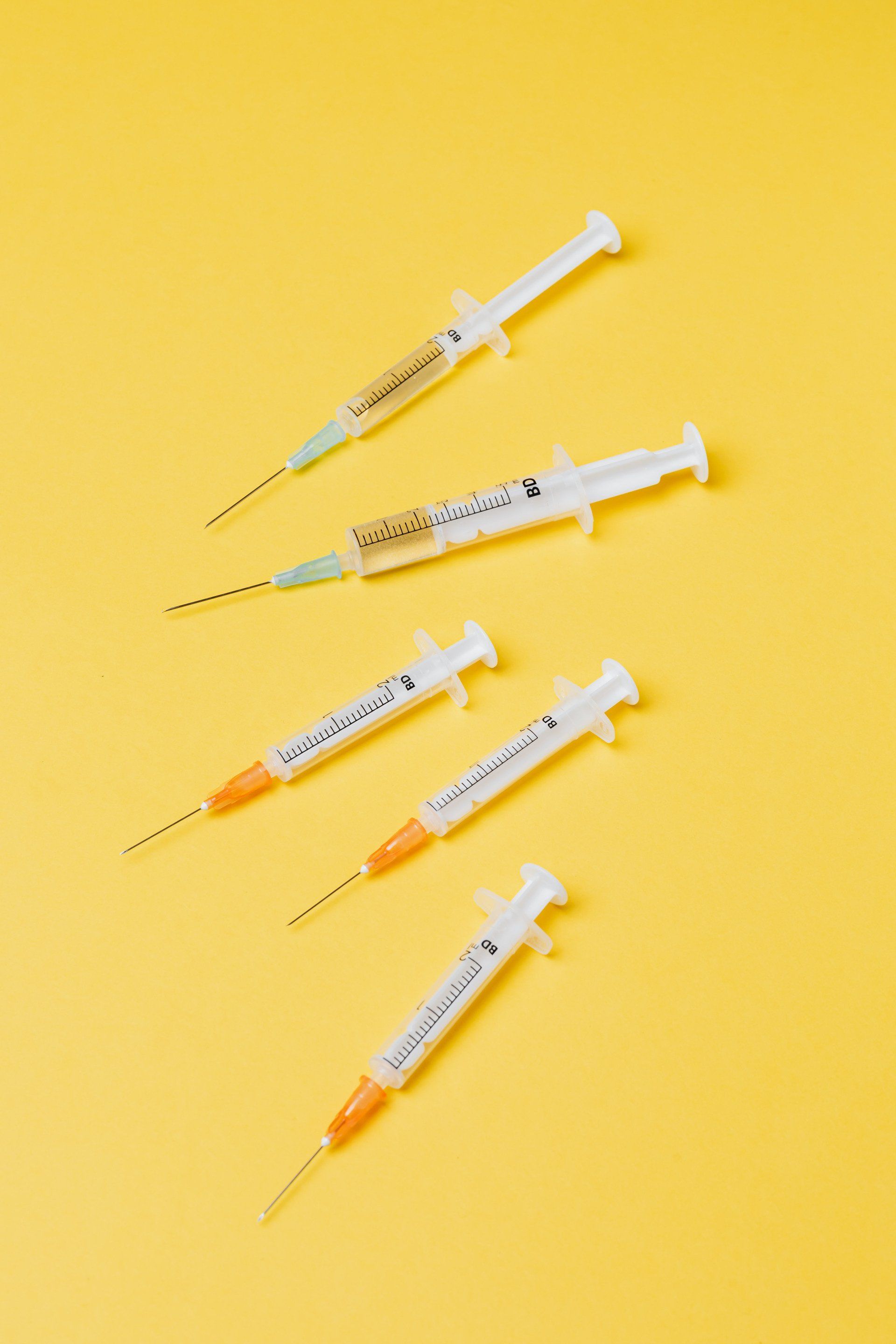 Four syringes are lined up in a row on a yellow background.