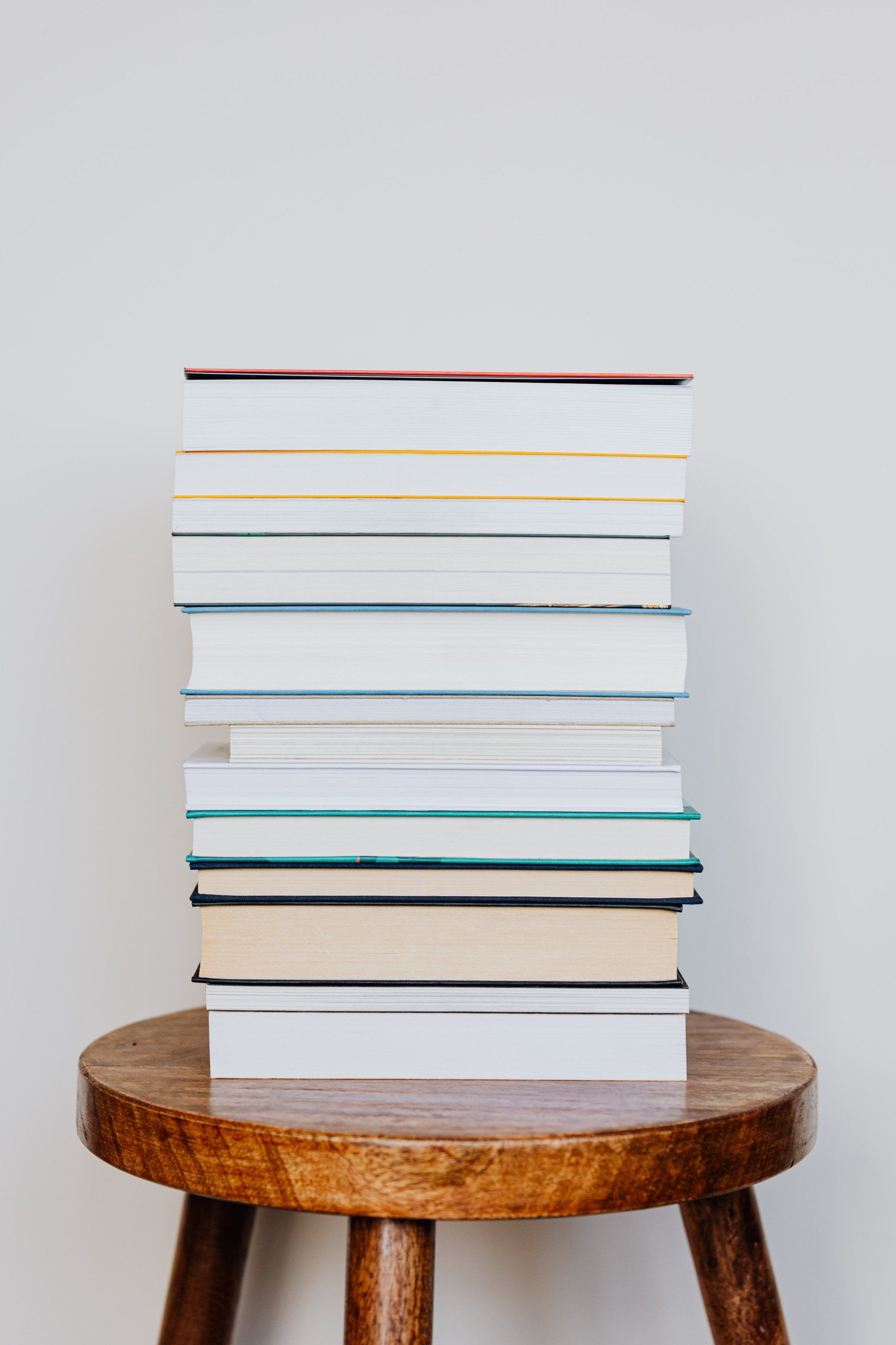 A stack of books is sitting on top of a wooden stool.