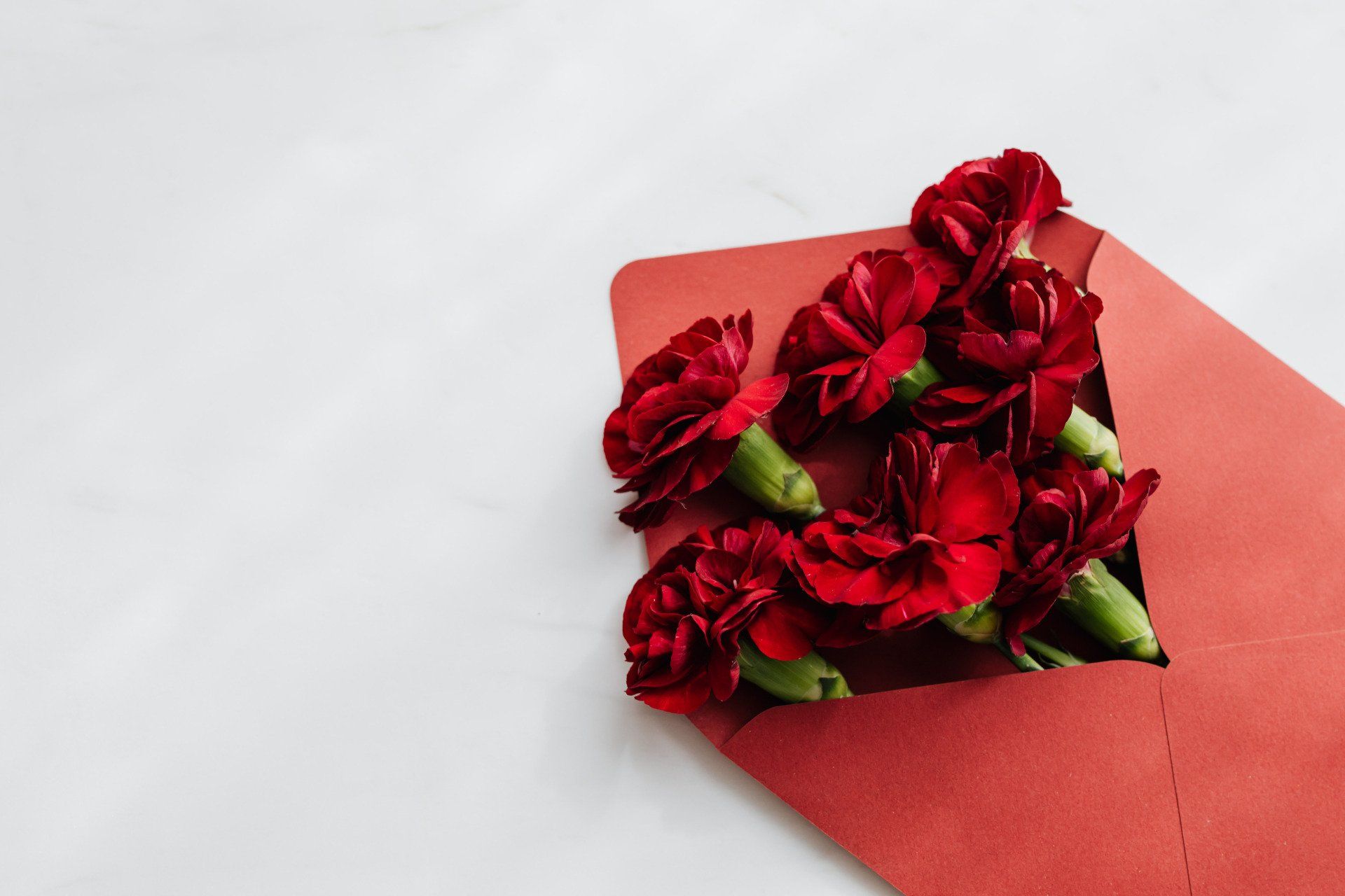 A red envelope filled with red flowers on a white surface.