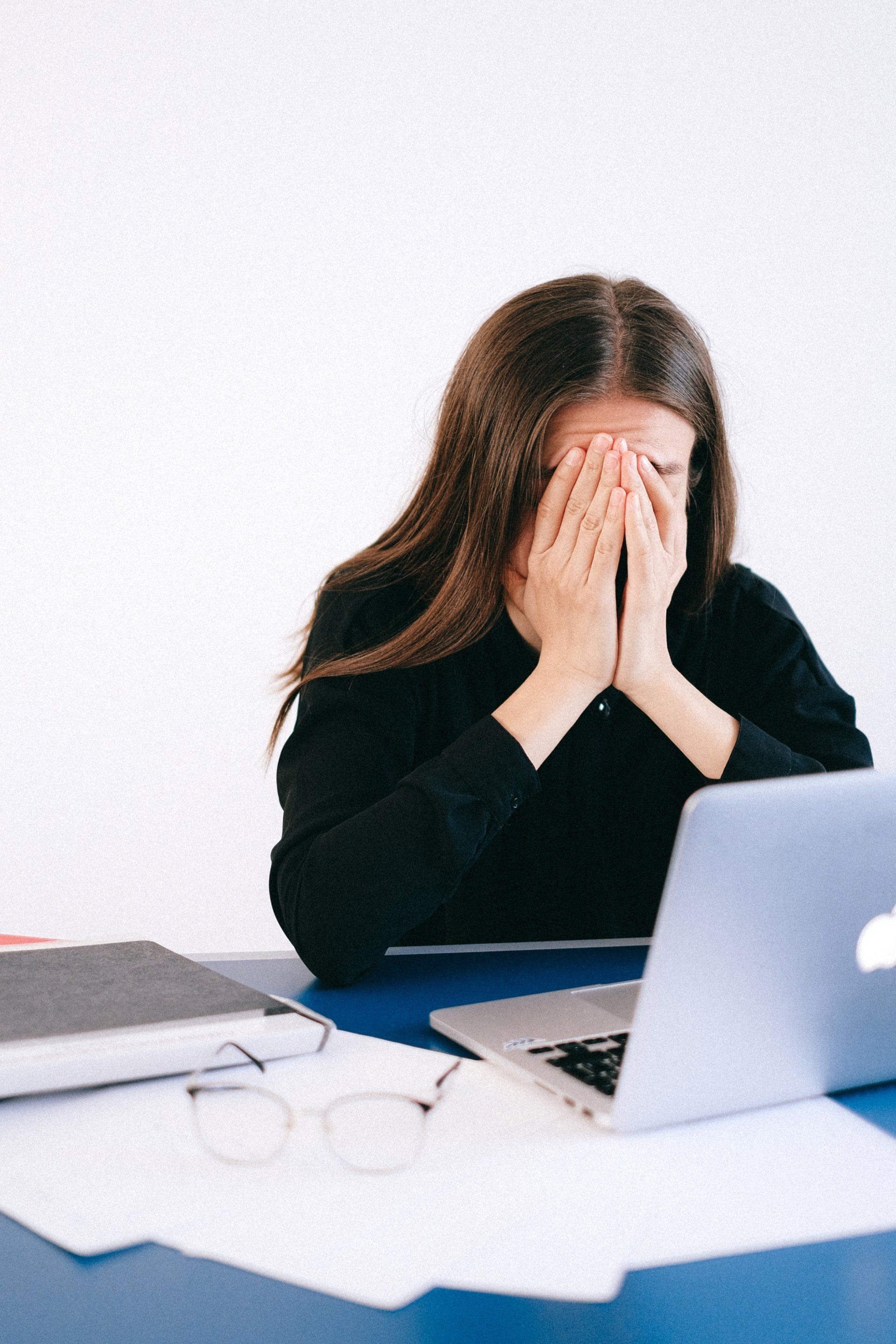 a woman covering her face with her hands in front of a laptop