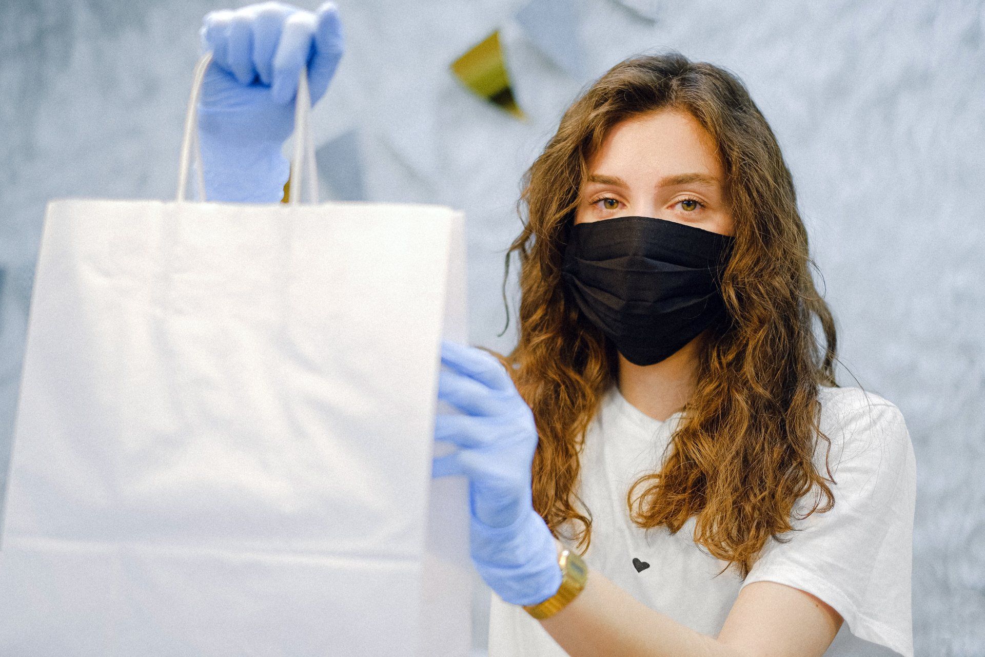 A woman wearing a mask and blue gloves is holding a paper bag.