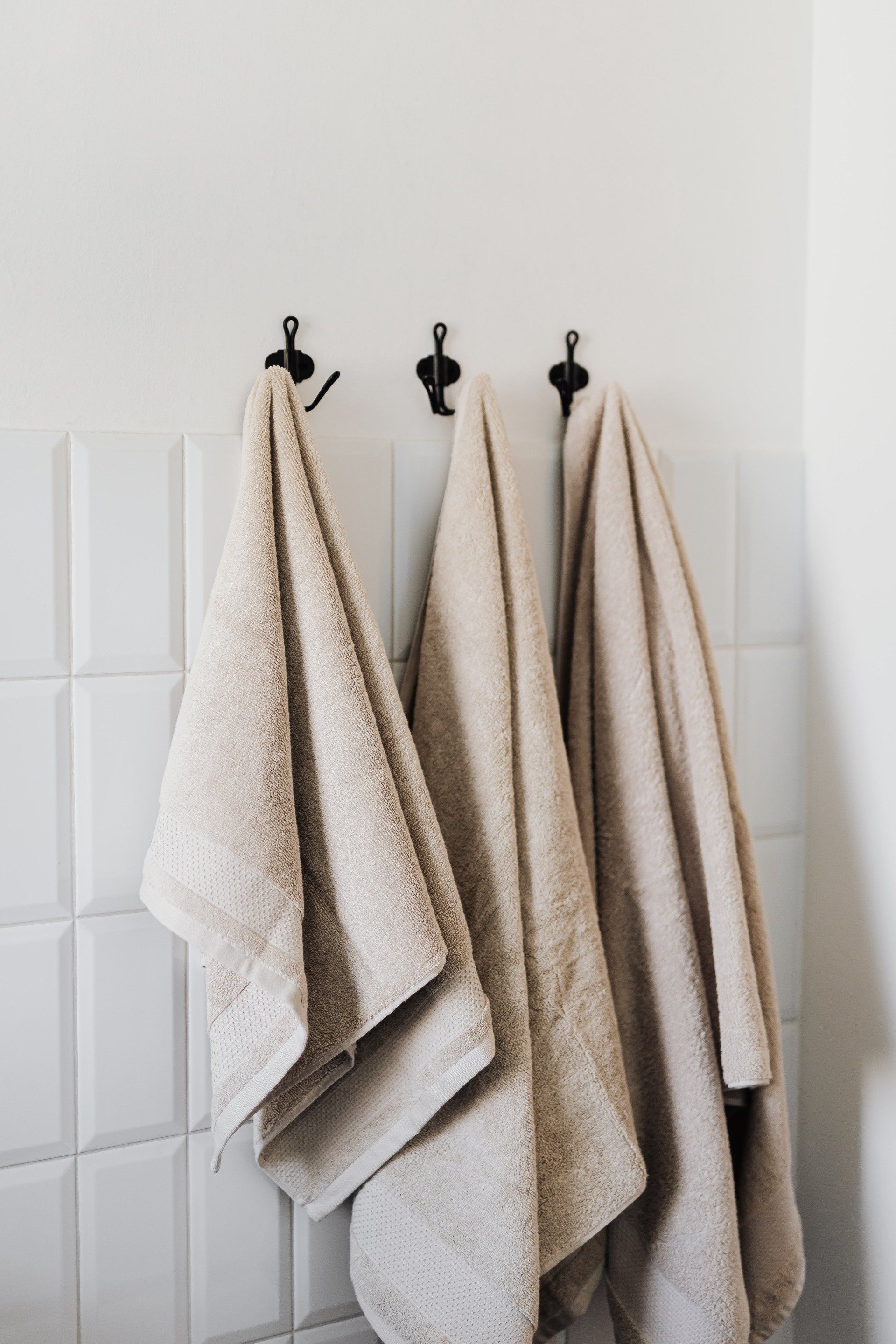beige handdukar på hängare med vitt kakel som fond