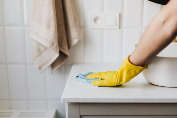A person wearing yellow gloves is cleaning a counter in a bathroom.