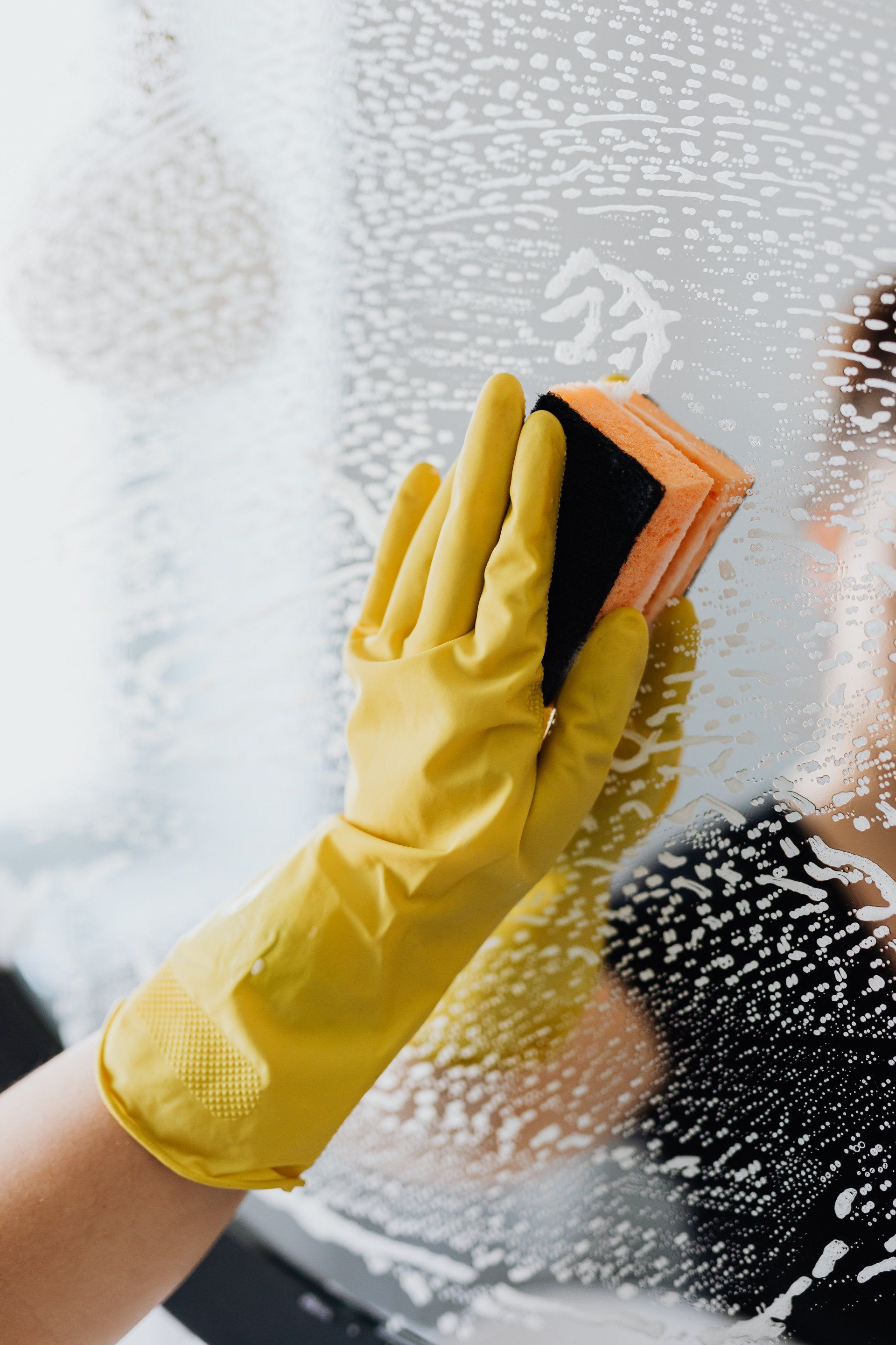 A person wearing yellow gloves is cleaning a window with a sponge.