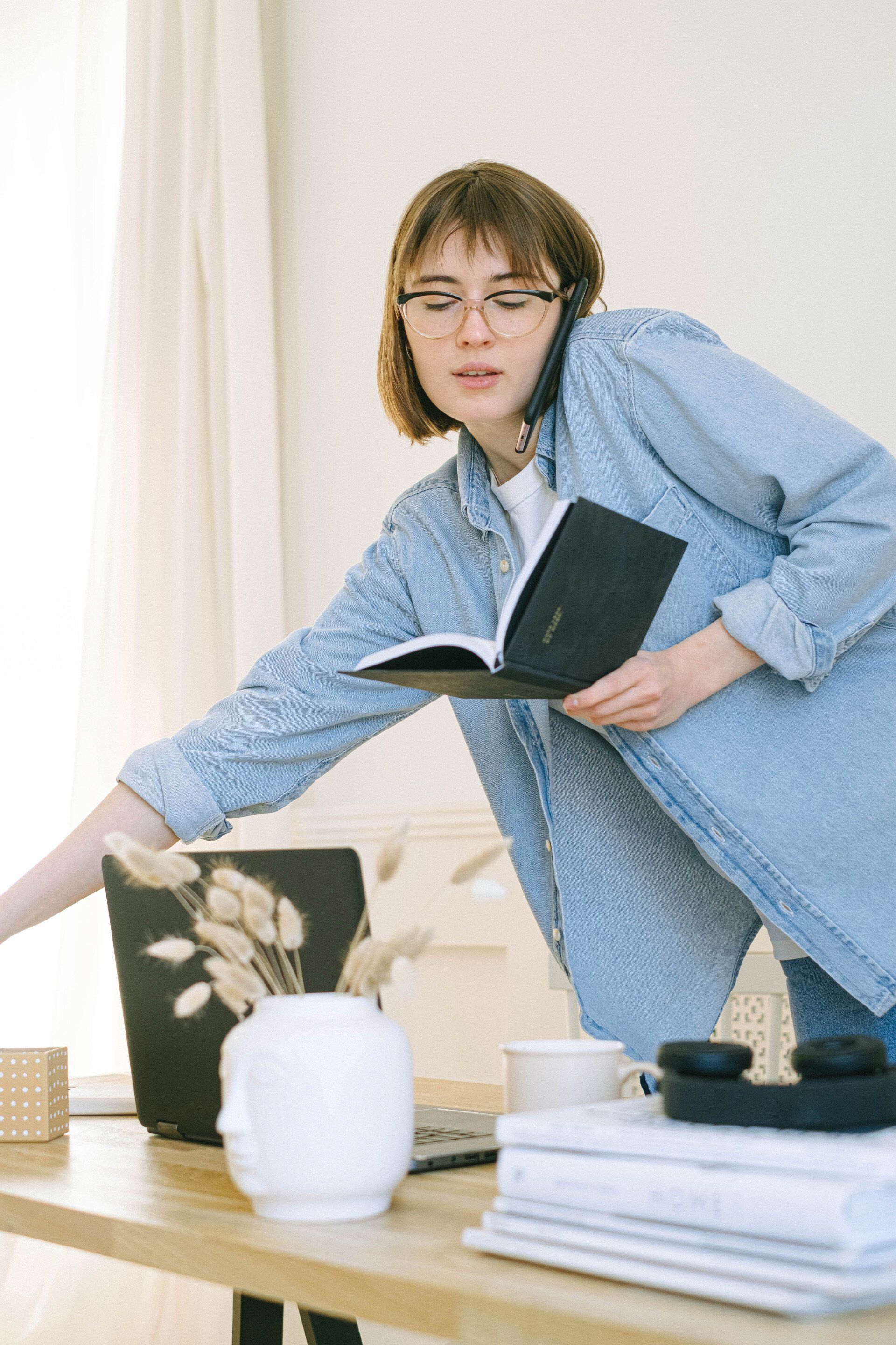 a woman is standing at a desk talking on a cell phone while holding a book .