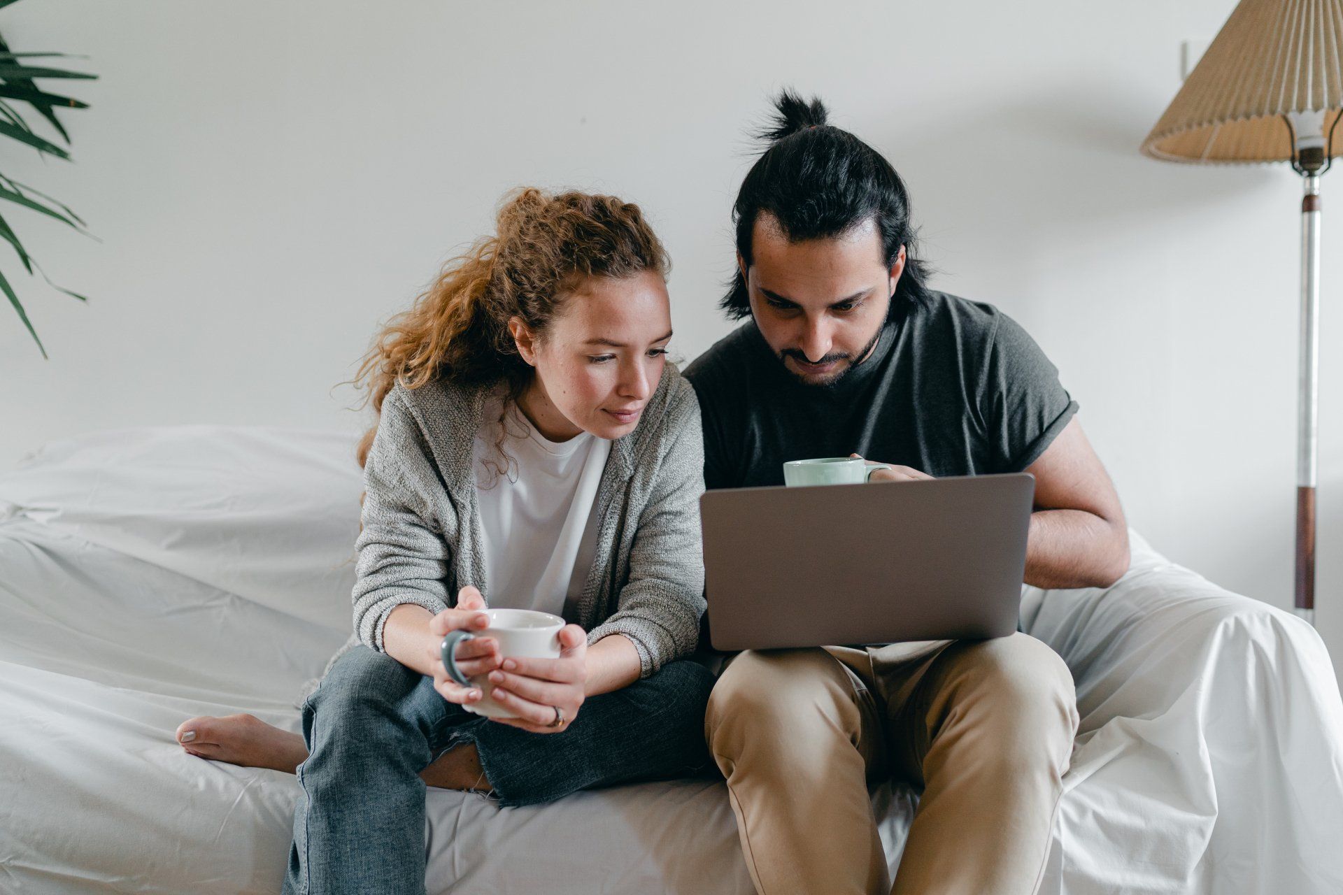 een man en een vrouw zitten op een bank en kijken naar een laptop.