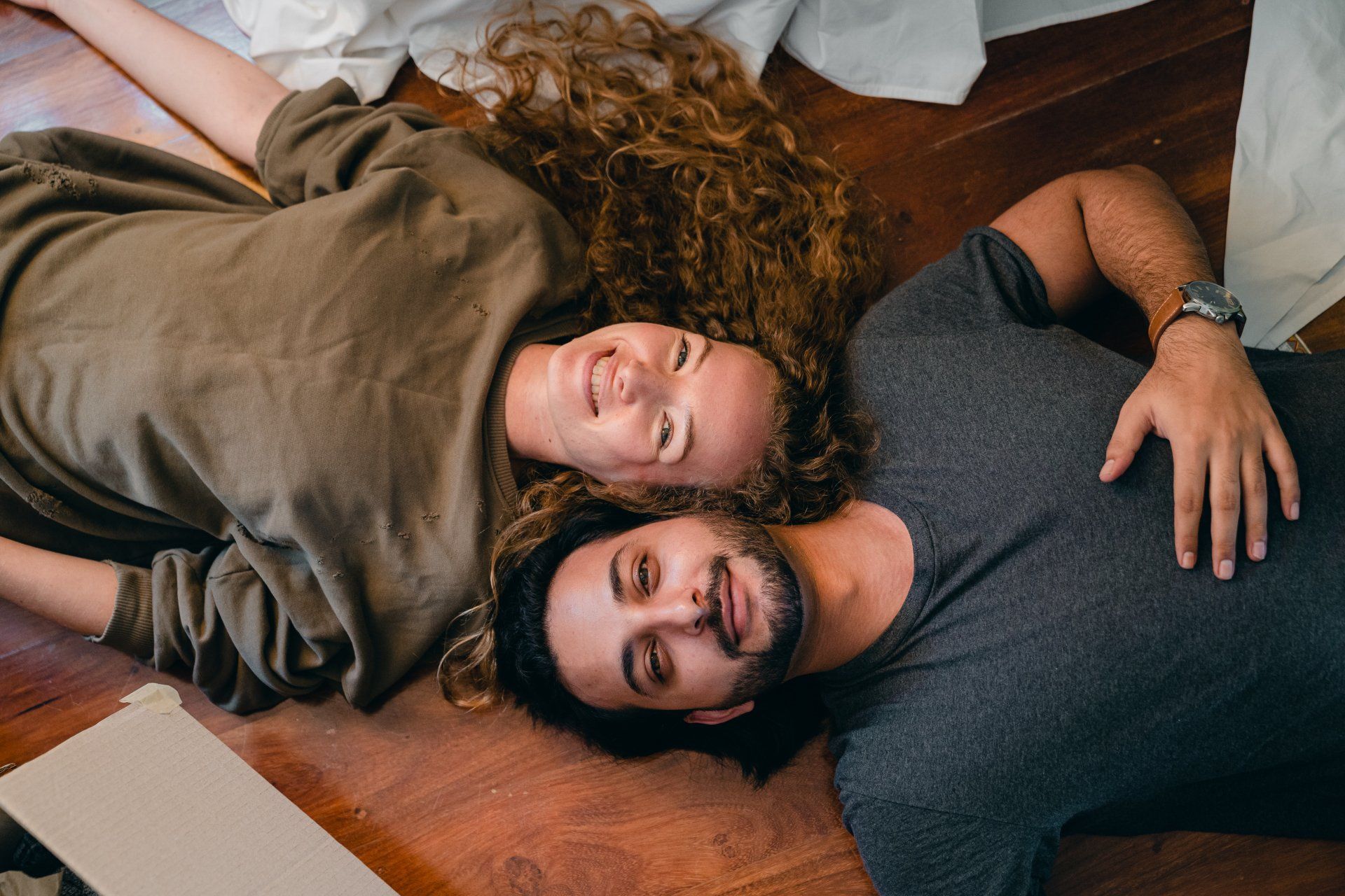 A man and a woman are laying on the floor with their heads together.