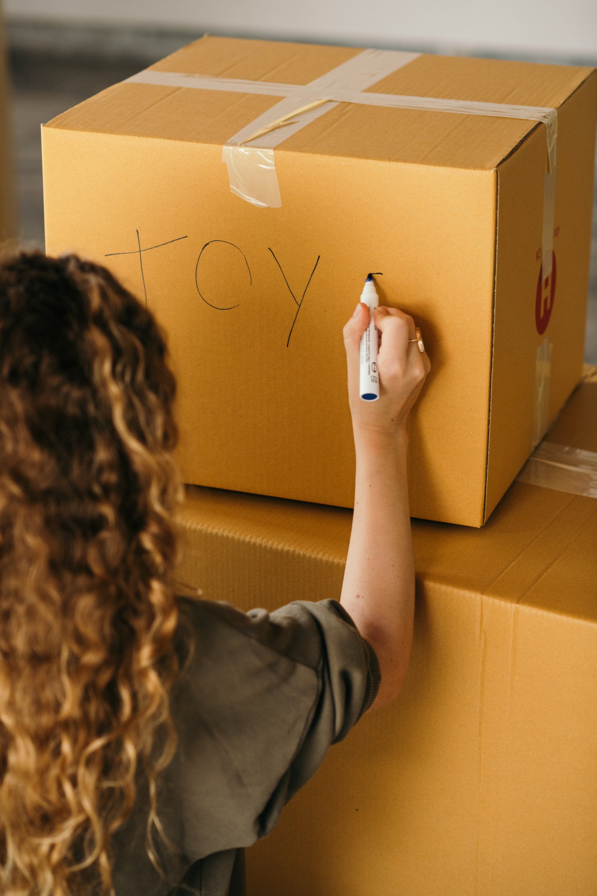 A woman is writing on a cardboard box with a marker.