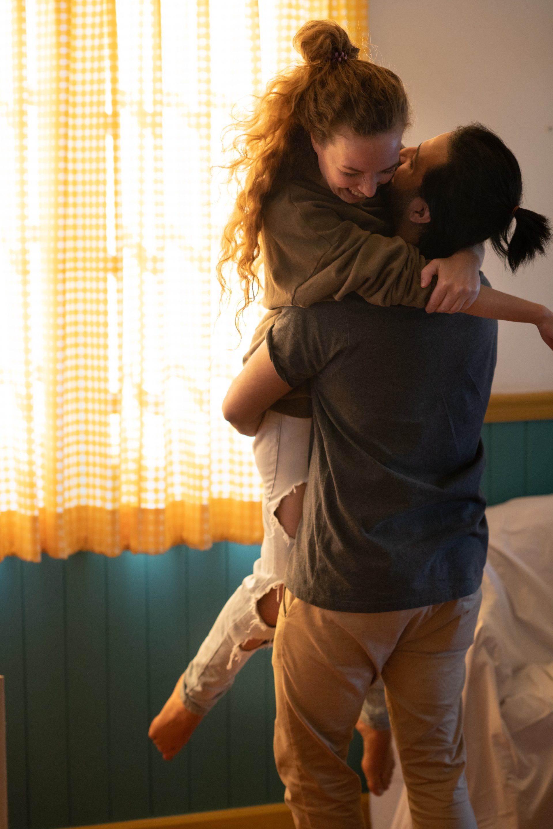 Two people hugging and lifting each other in a warmly lit room near a curtained window