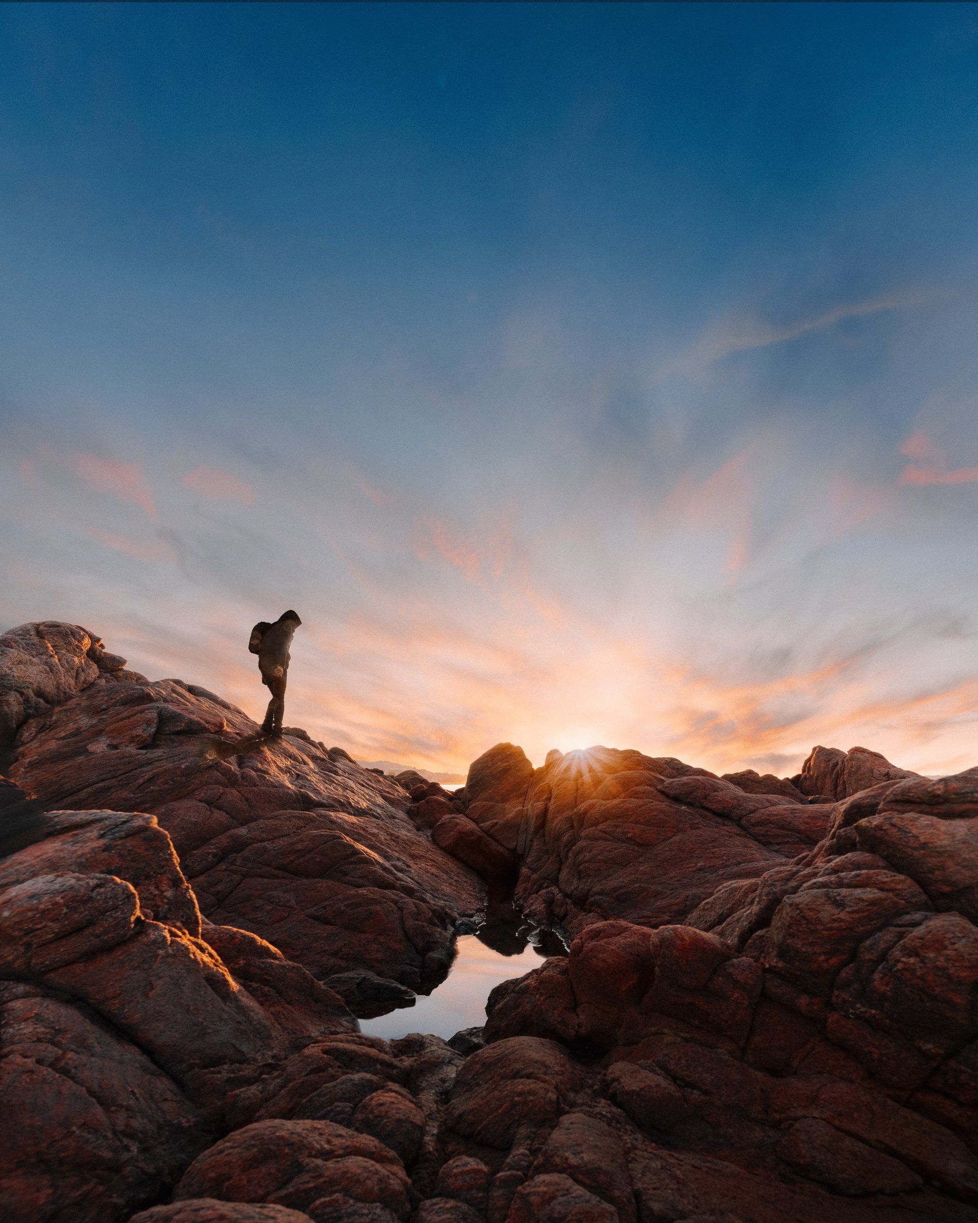 a person is standing on top of a rocky hill at sunset .