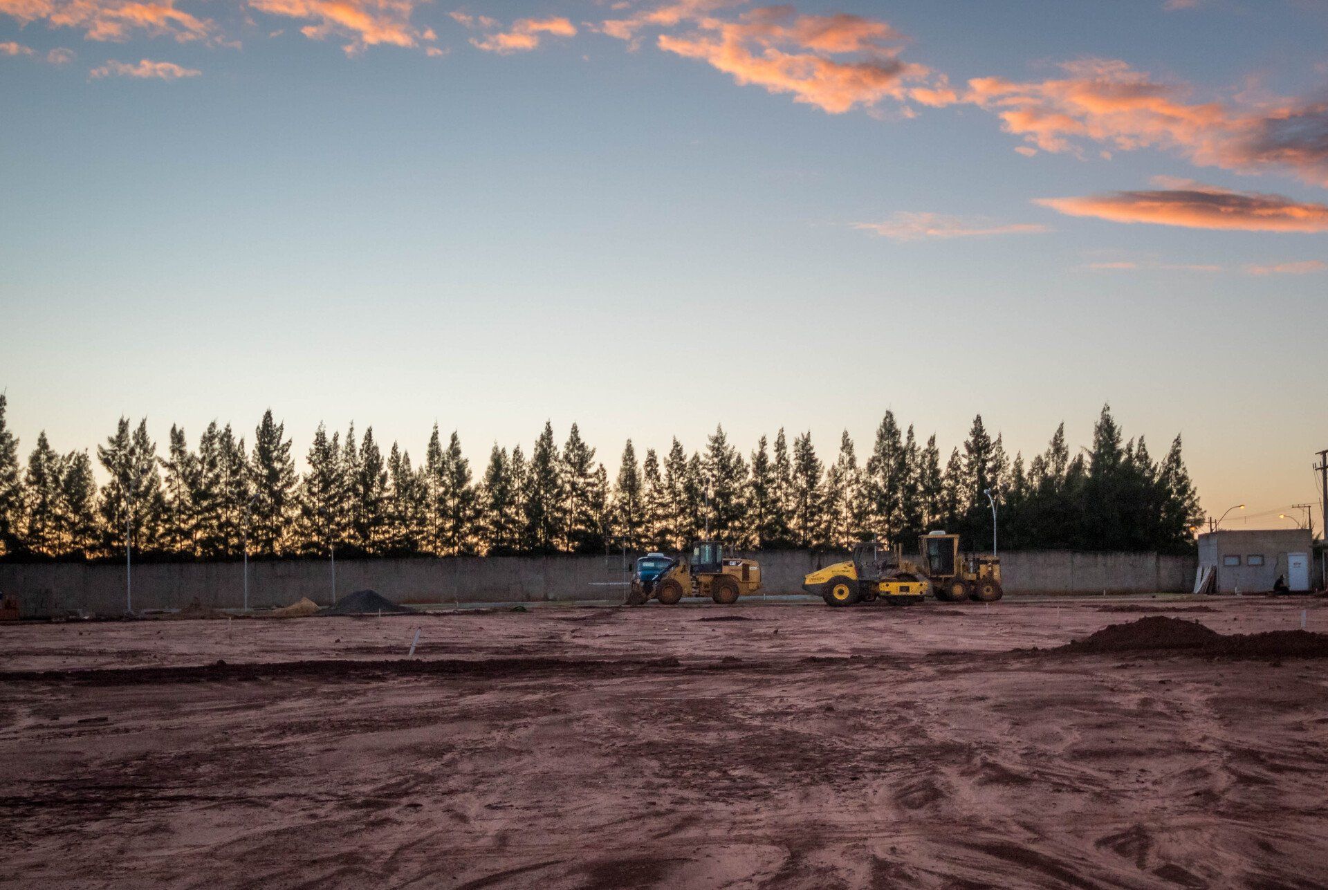 a row of construction vehicles are parked in a dirt field