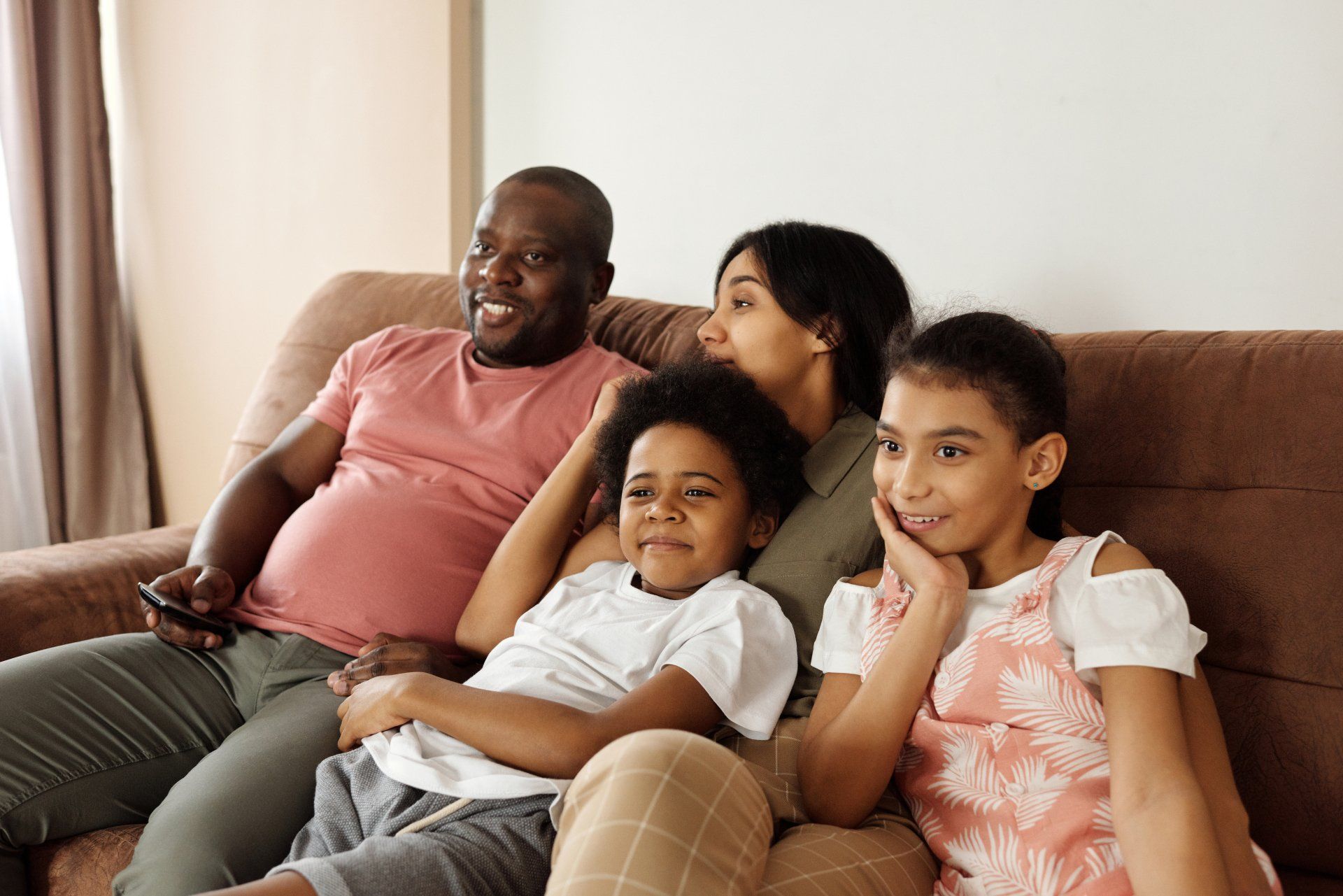 A family is sitting on a couch watching tv together.