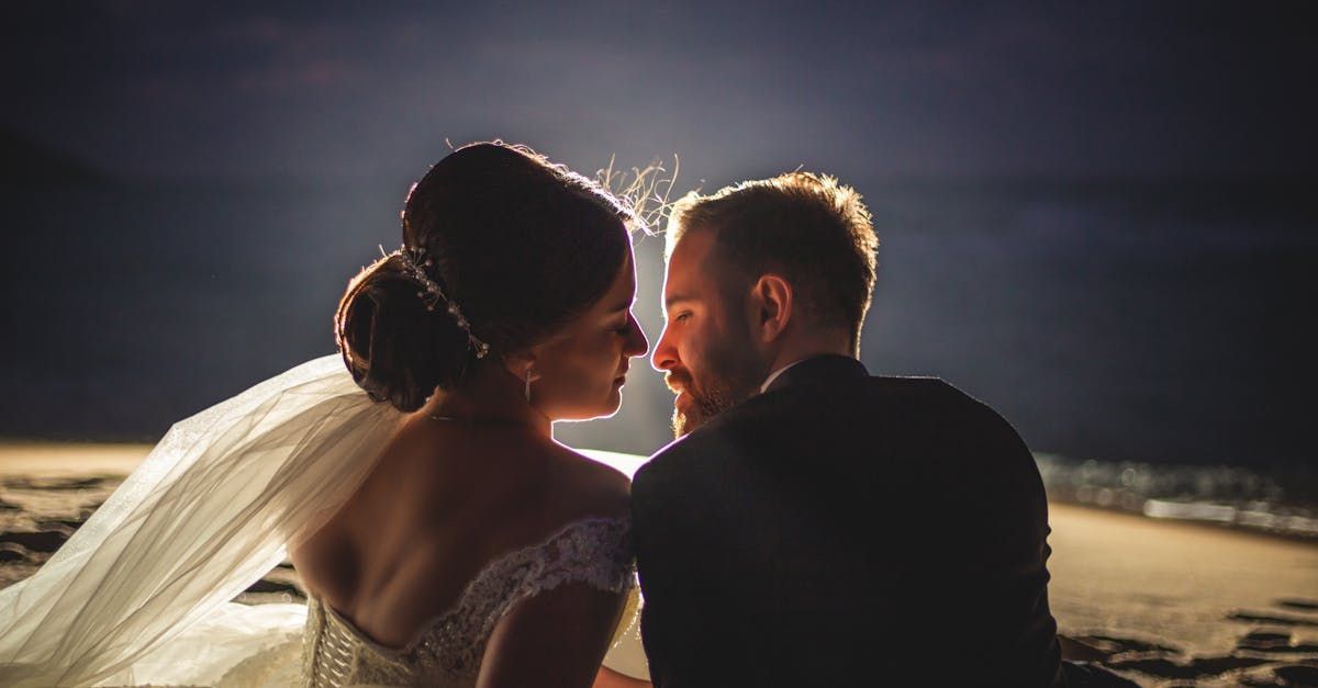 Backlit couple in wedding attire sharing a close moment on a beach at dusk