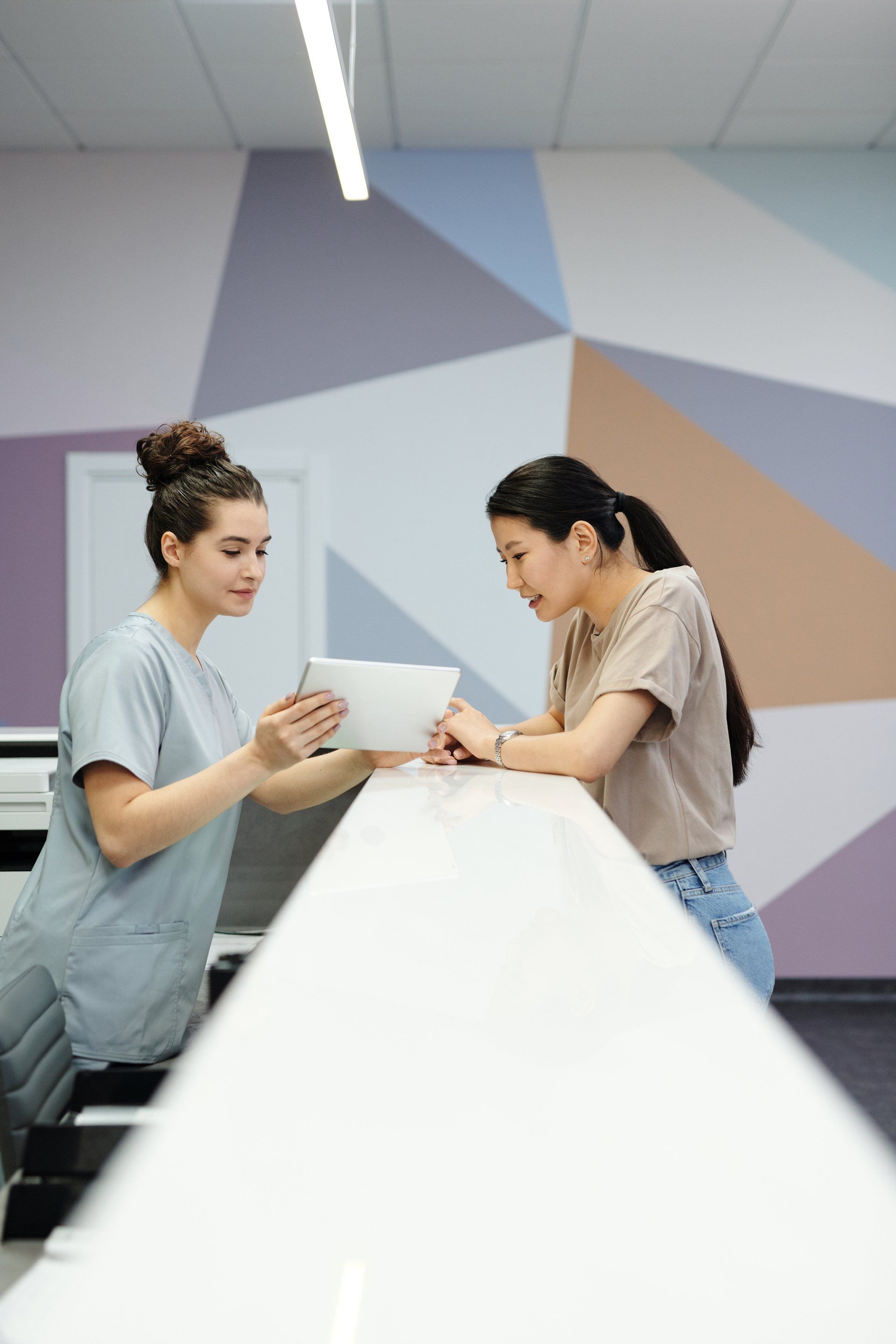 Deux femmes sont debout à un comptoir et regardent une tablette.