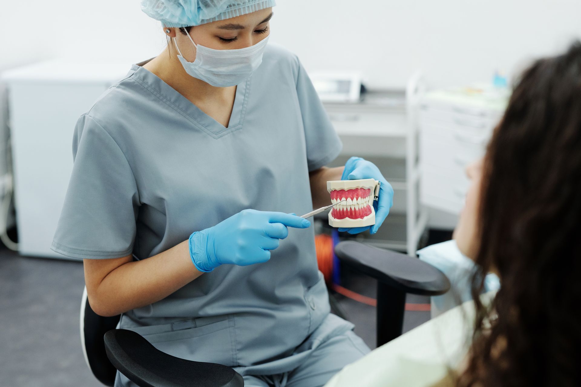 Dentist in scrubs showing a teeth model to a patient in a dental office.