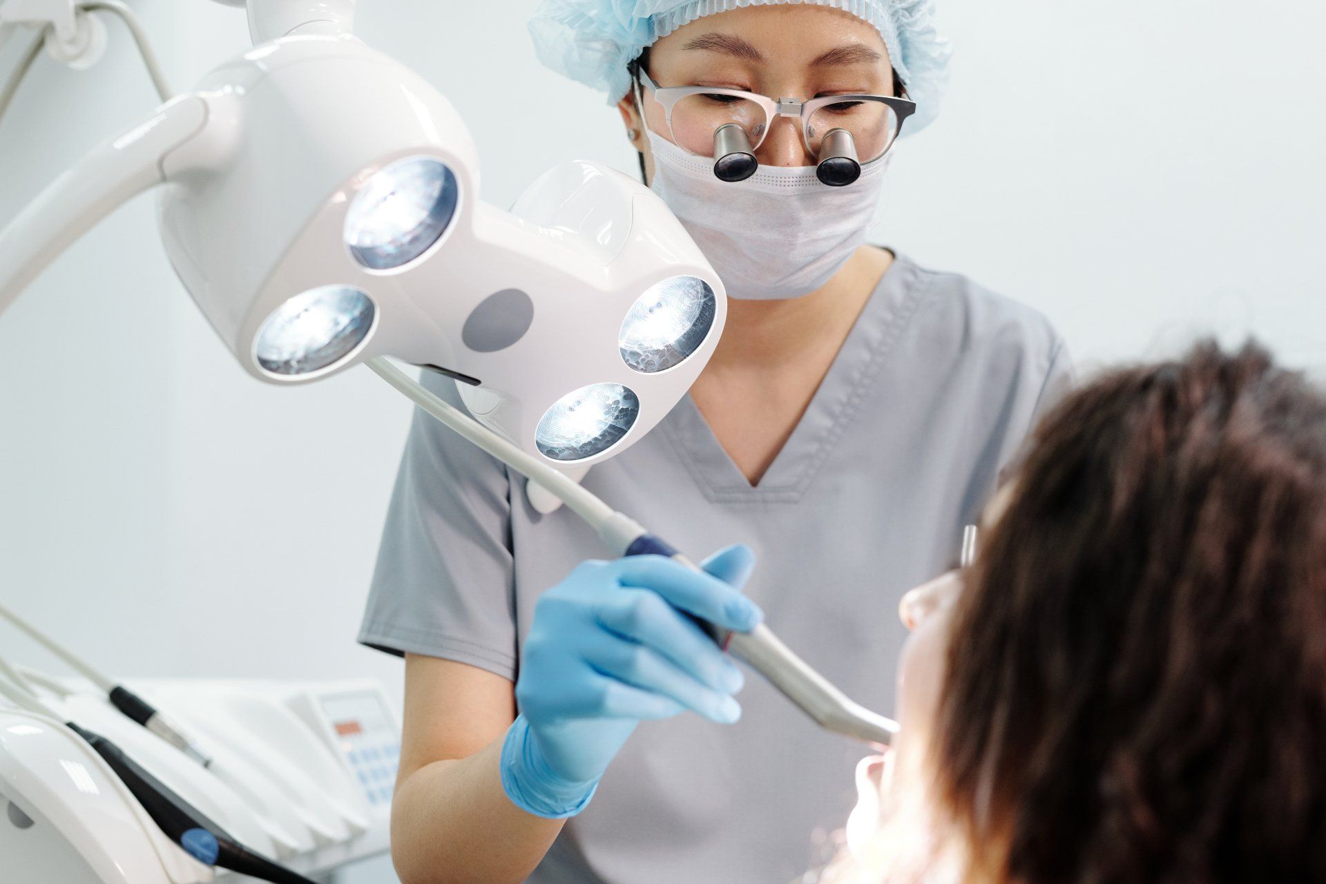 Dentist examining a patient's mouth under bright light; dental office setting.
