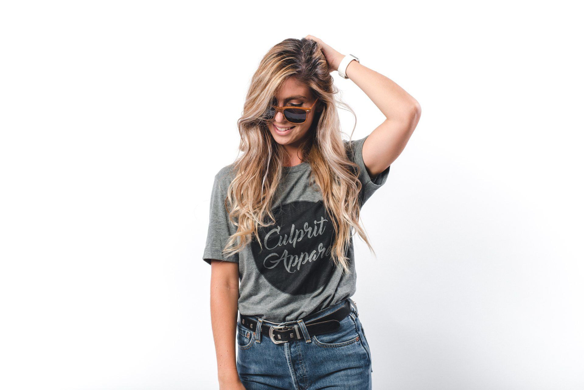 Een vrouw met een zonnebril en een t-shirt staat voor een witte muur.